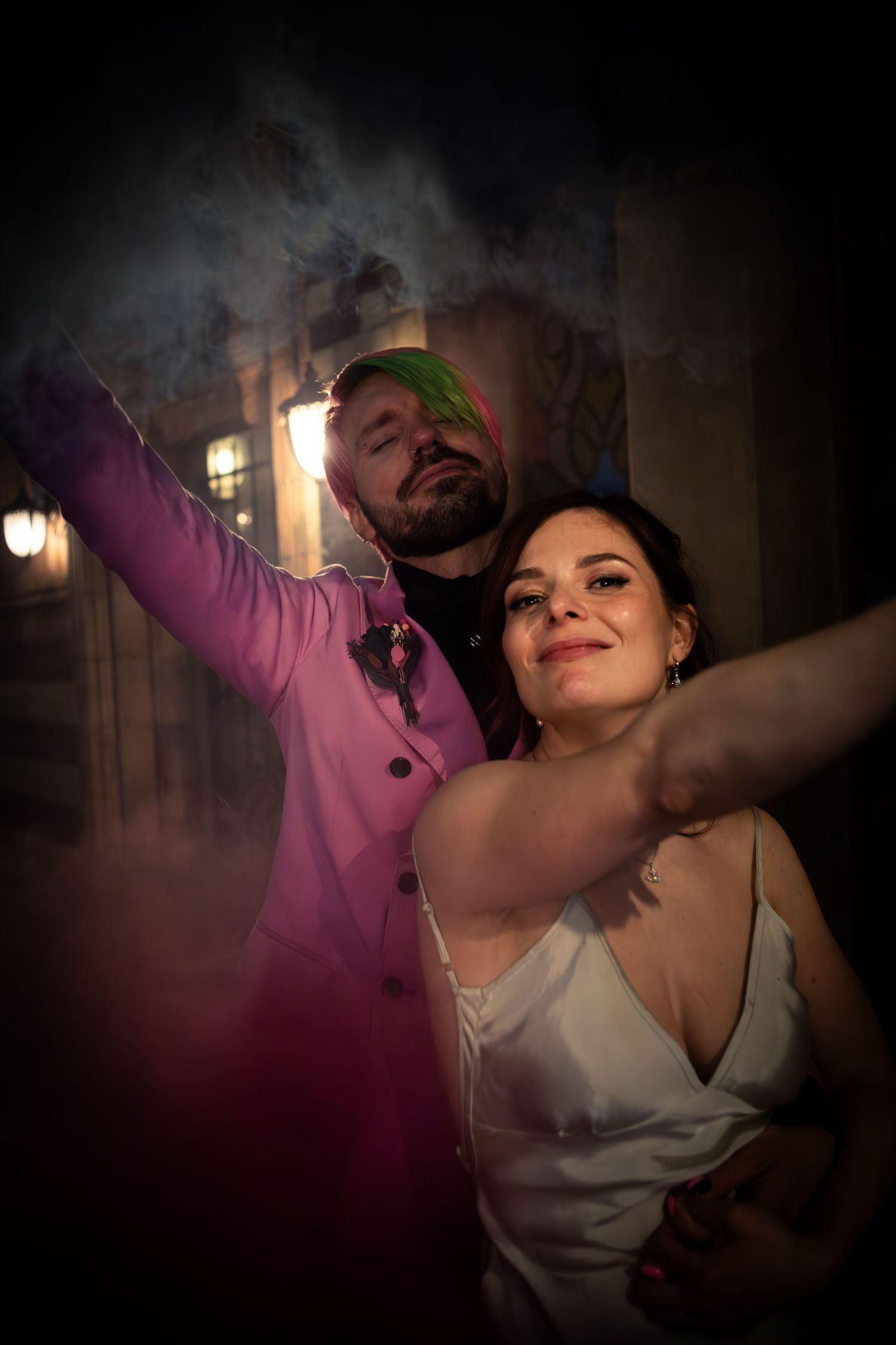 A couple dances intimately at a dimly lit indoor venue with atmospheric smoke and warm lighting in the background.