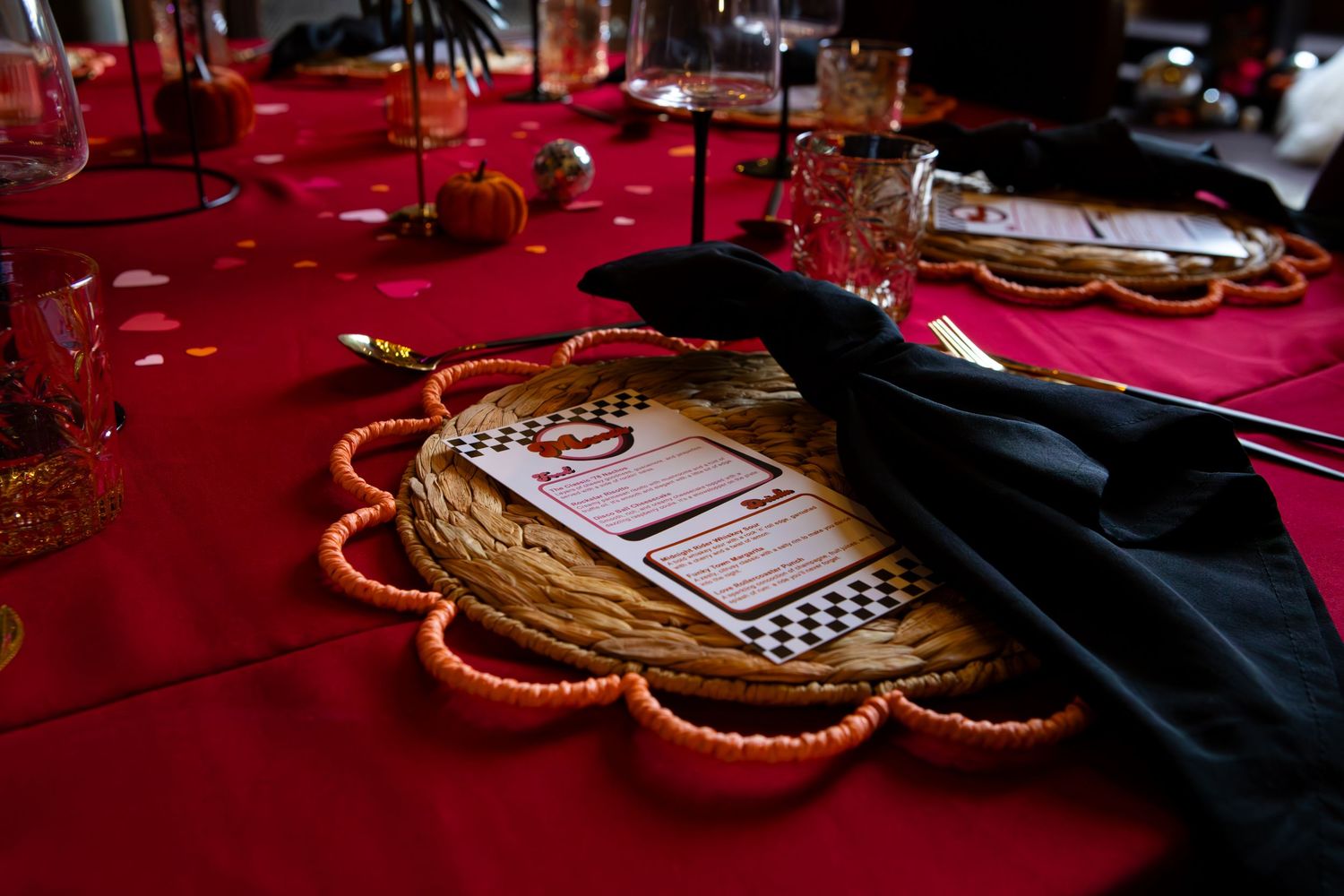 Elegant table setting with gold scalloped plate on red tablecloth with black napkin at formal dinner event.