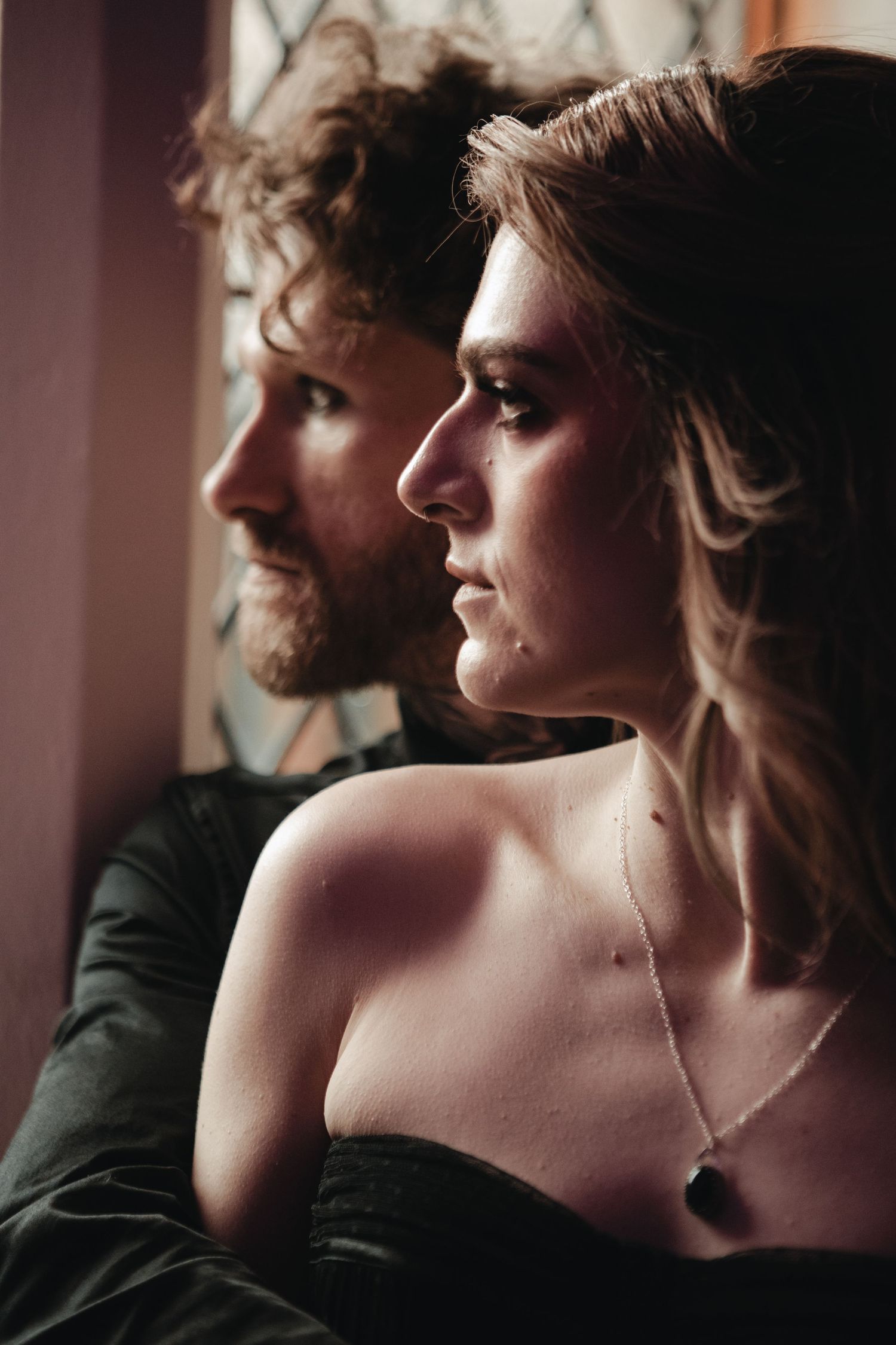 Side profile portrait of two people in intimate pose with soft lighting and moody atmosphere.