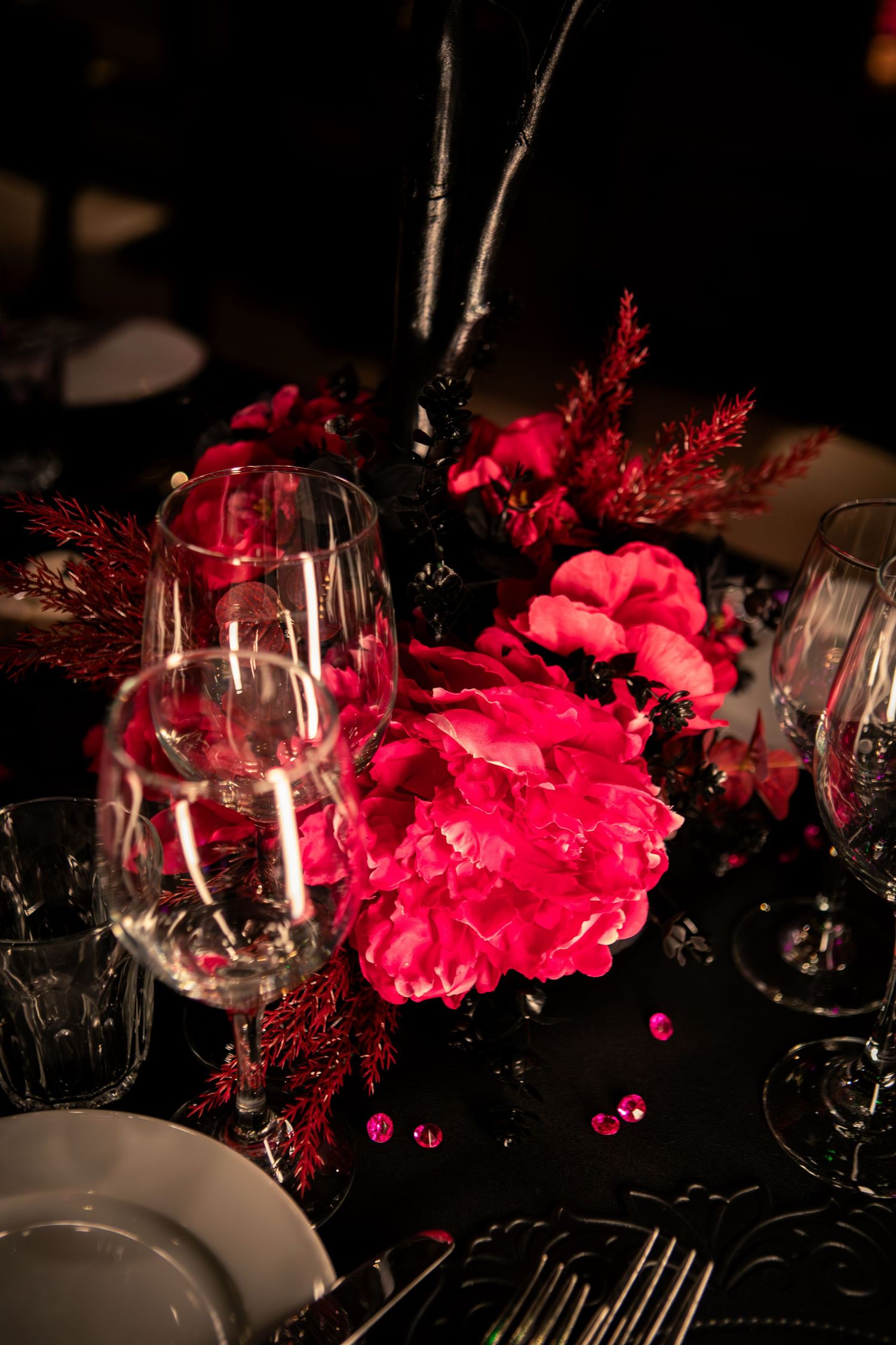 Elegant table setting with bright pink floral centerpieces, wine glasses, and black tablecloths create a dramatic ambiance.