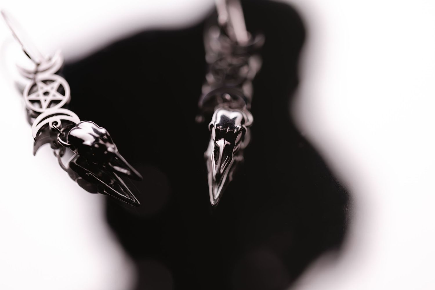 Two silver bird skull pendants in black and white artistic photo casting shadows against dark background.