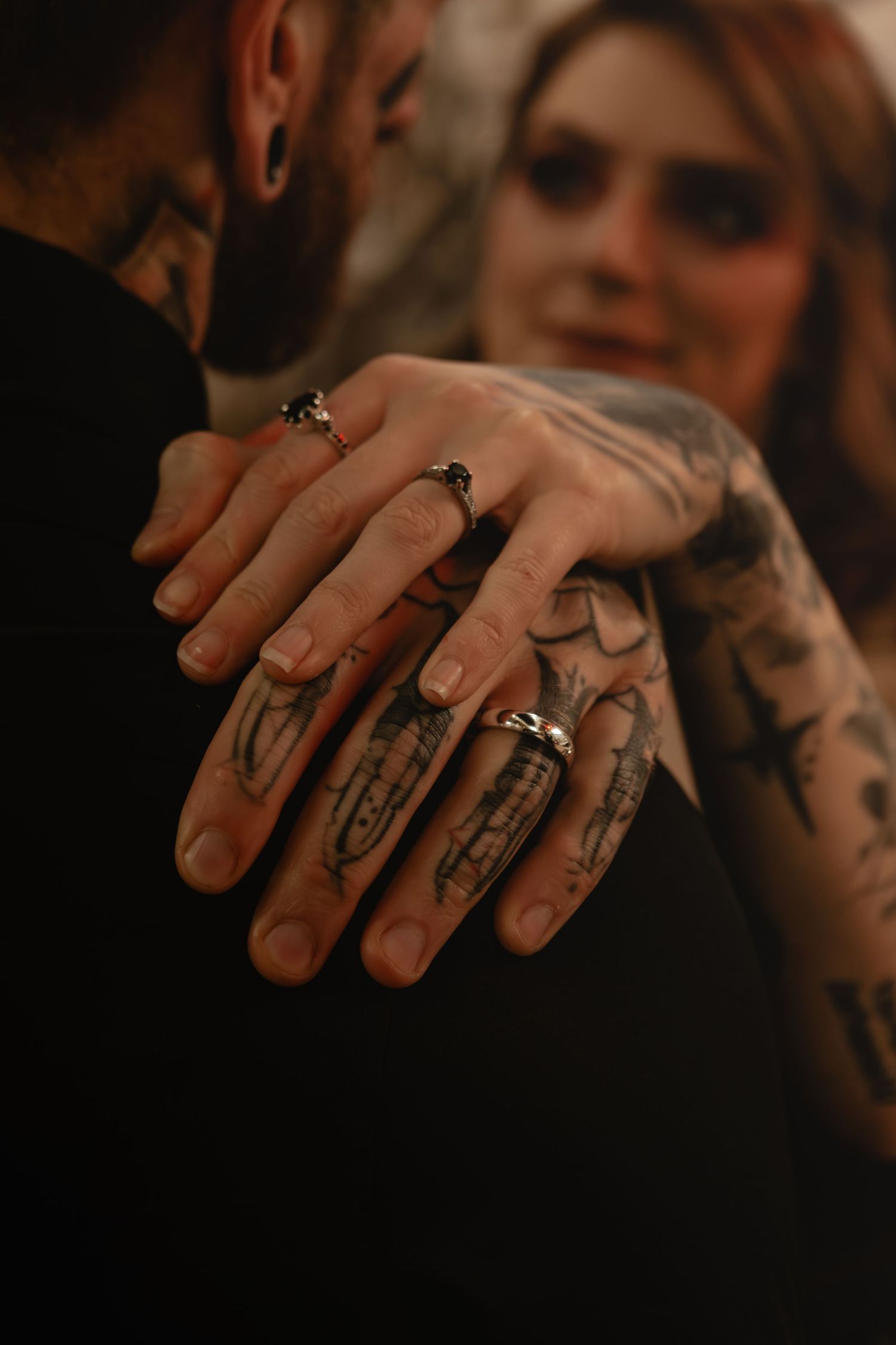 Close-up of tattooed hands with rings touching in a romantic moody setting.