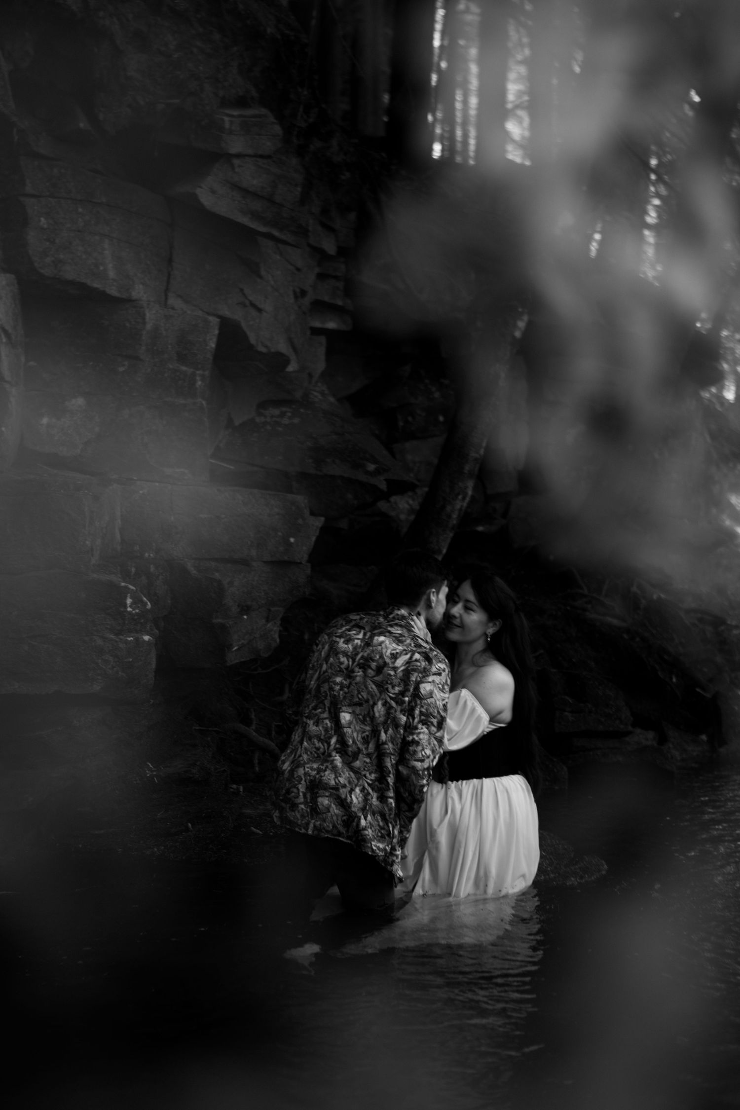 A black and white artistic photo of a couple in water with dramatic lighting.