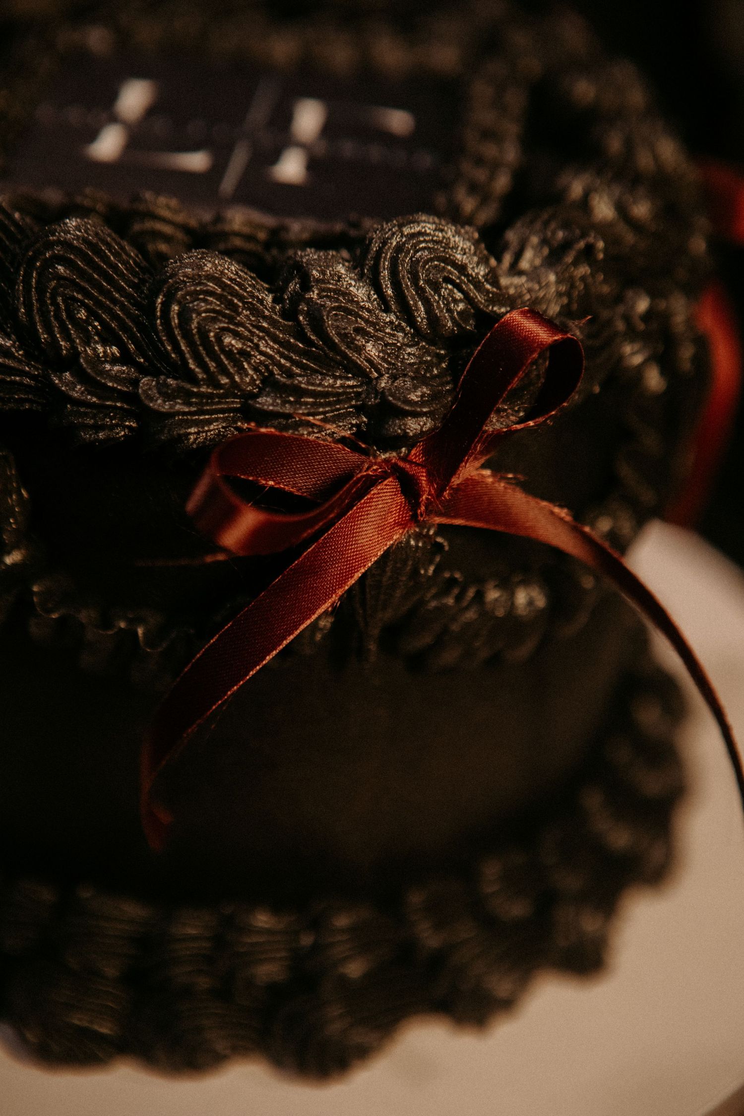 Close-up detail of black lace trim with burgundy ribbon bow decoration against dark background.