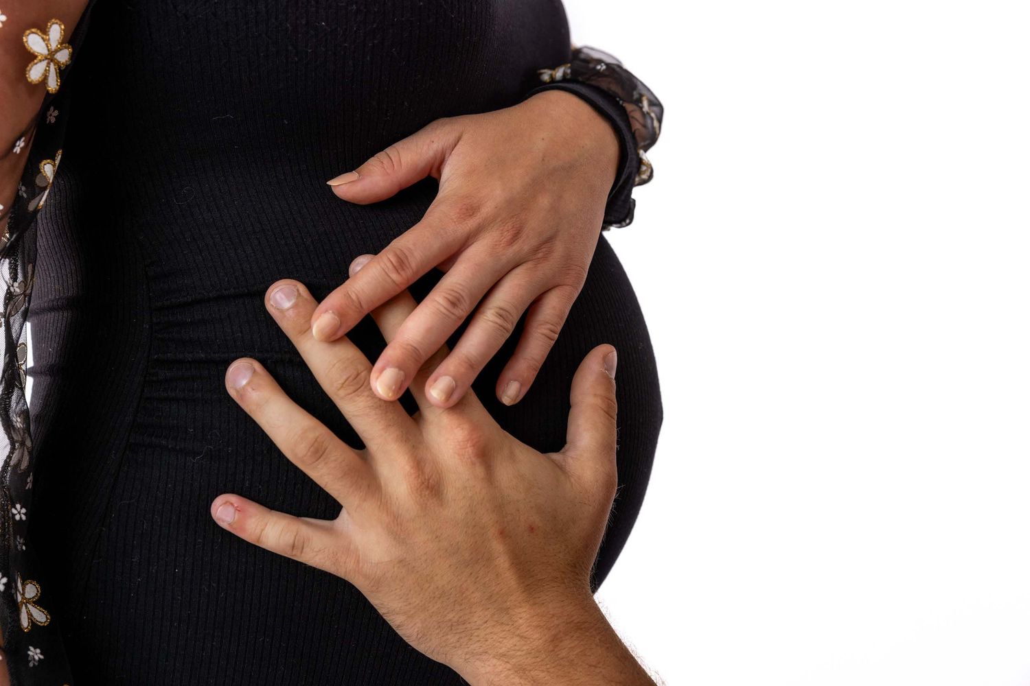 Close-up of hands resting on a pregnant woman's belly shown against a black background.