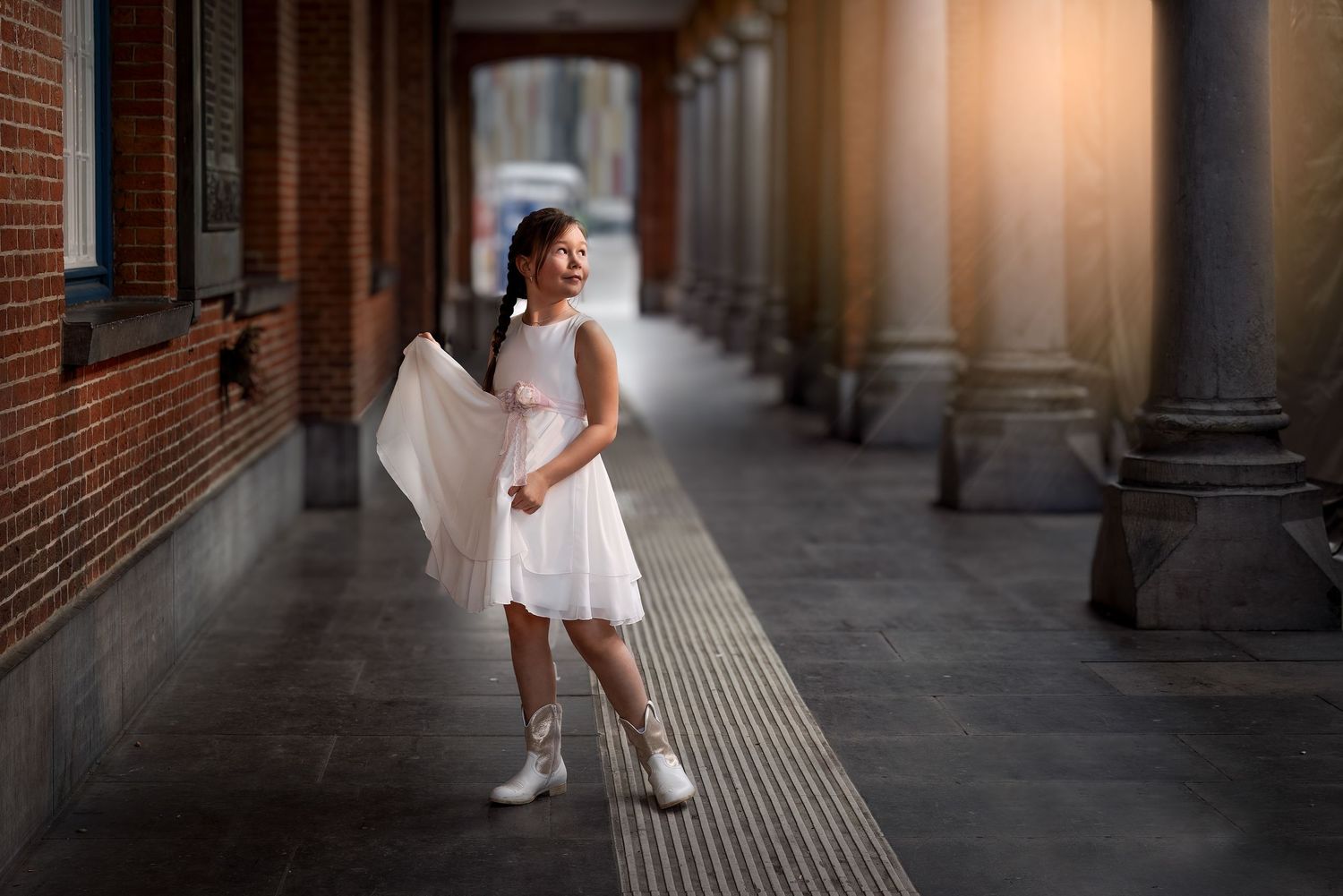 A young figure in a white dress and headpiece stands in a columned hallway with dramatic lighting.