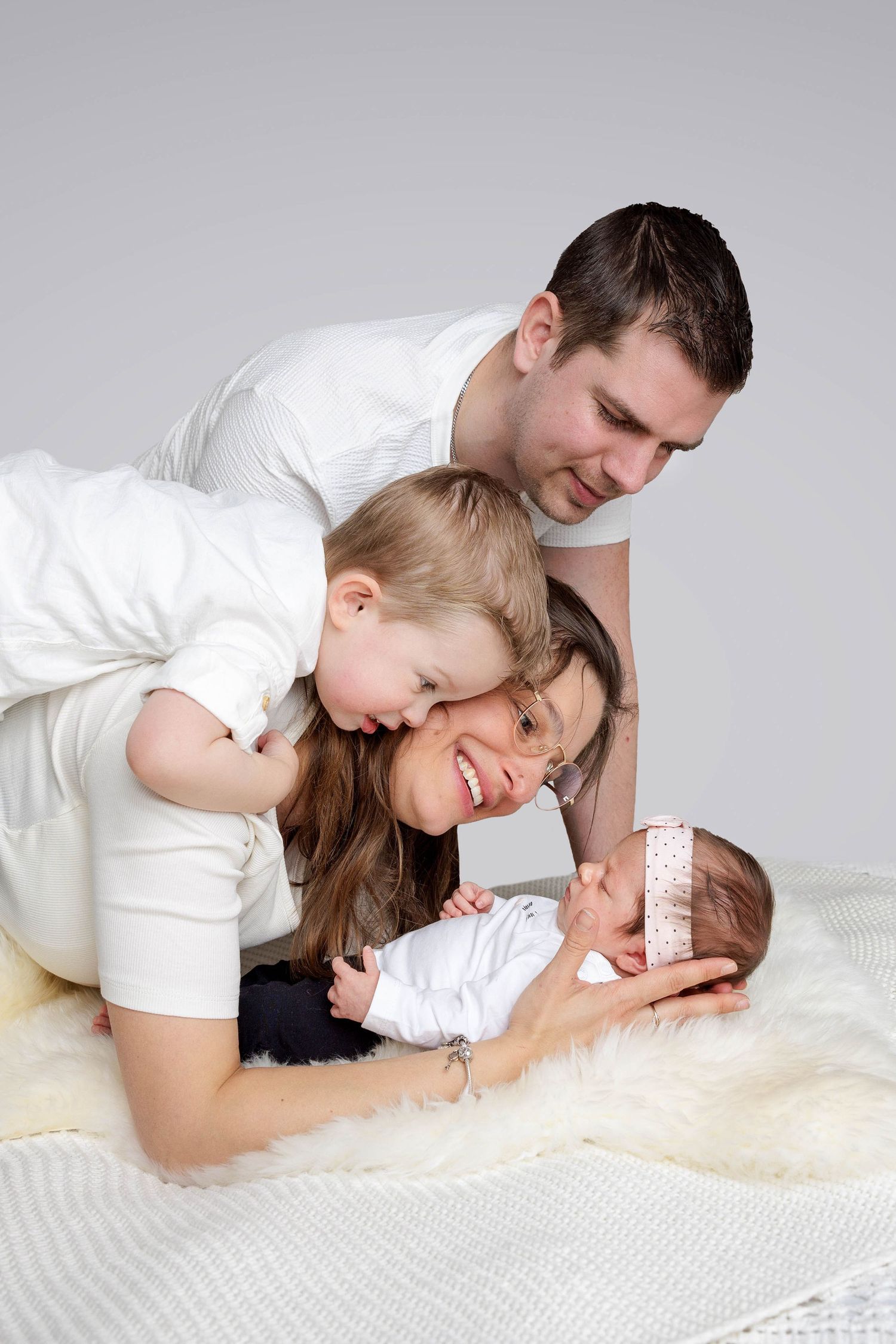A loving family moment captured on white bedding as they snuggle together with their newborn baby.