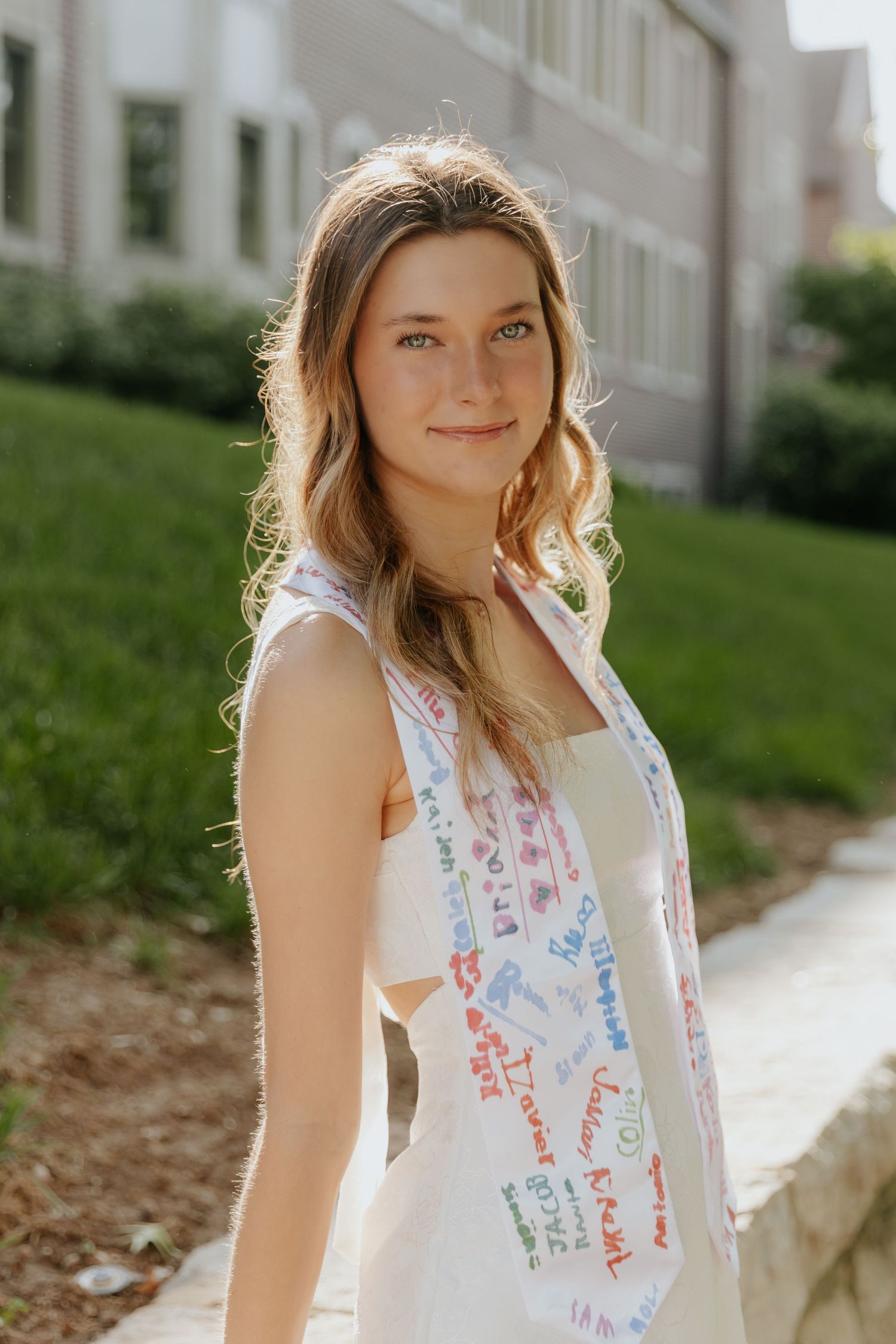 Portrait taken outdoors showing someone in a white dress with colorful text prints in natural sunlight.
