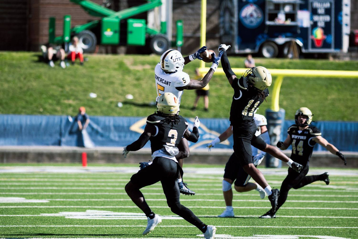Football players compete for a catch during an intense game on the field with bright green turf.