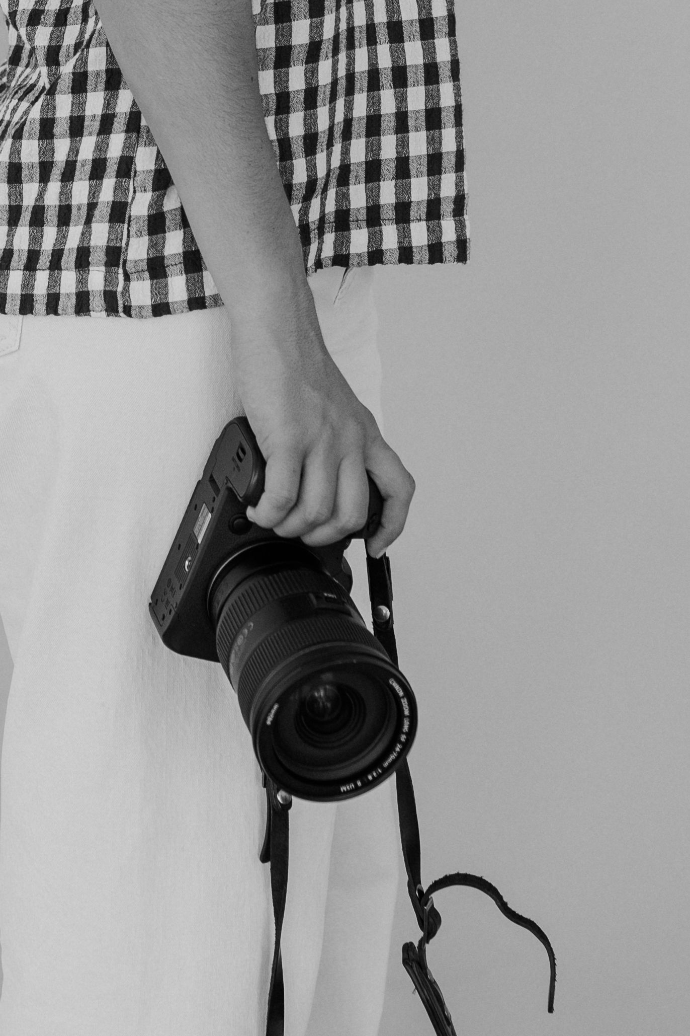 A hand holds a professional digital camera with a wide-angle lens against a black and white gingham pattern background.
