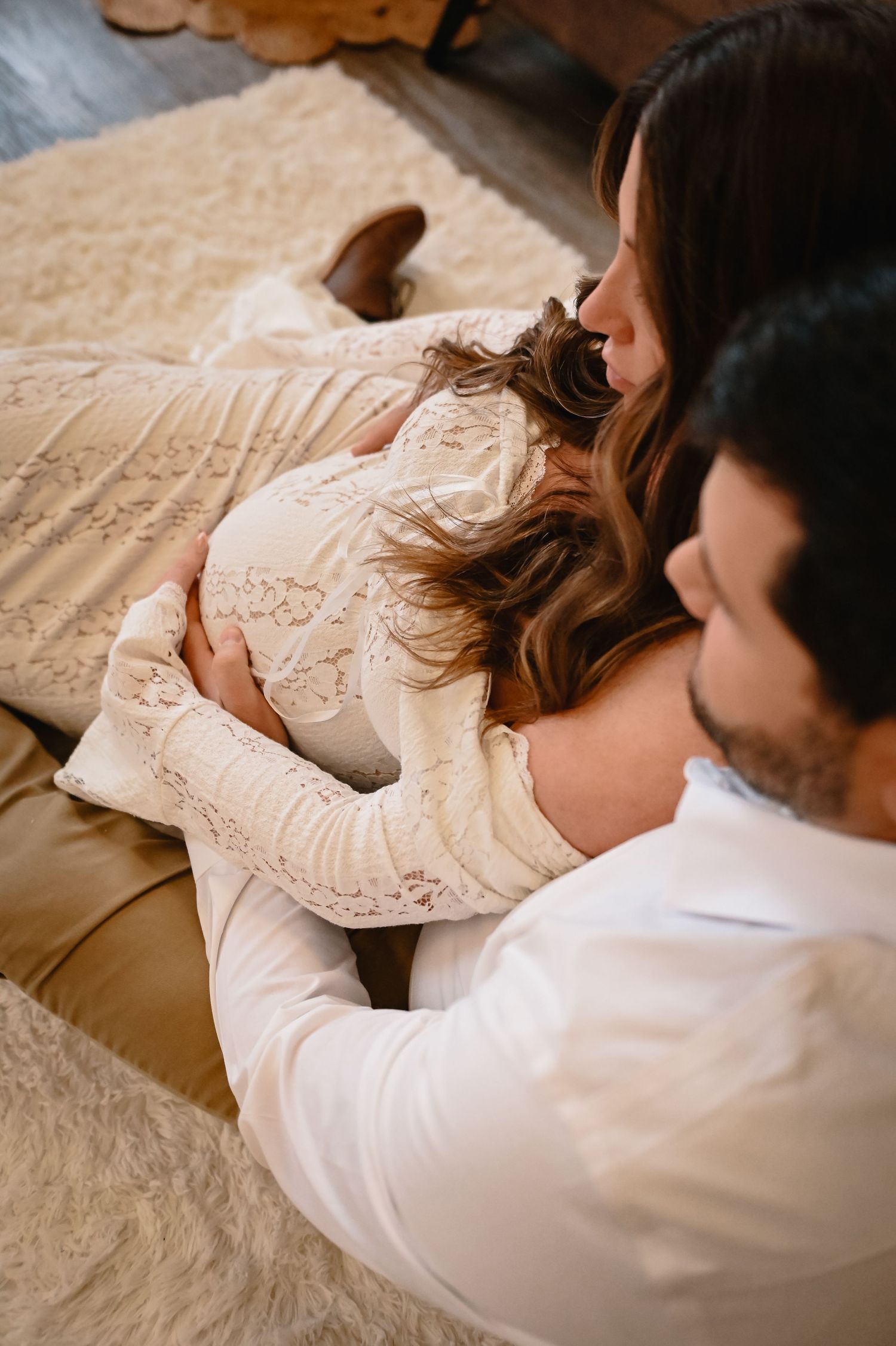 Side view of maternity couple photos in white lying on white bedding in an intimate romantic moment.