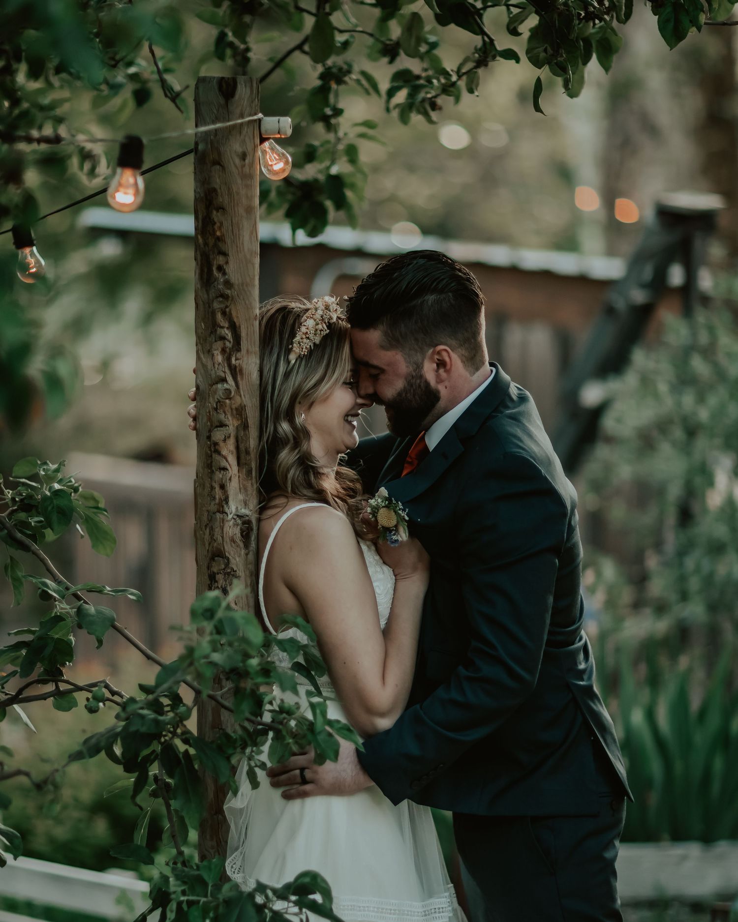 A romantic moment captured cinematically between a couple embracing outdoors with soft bokeh lights and lush greenery surrounding them.