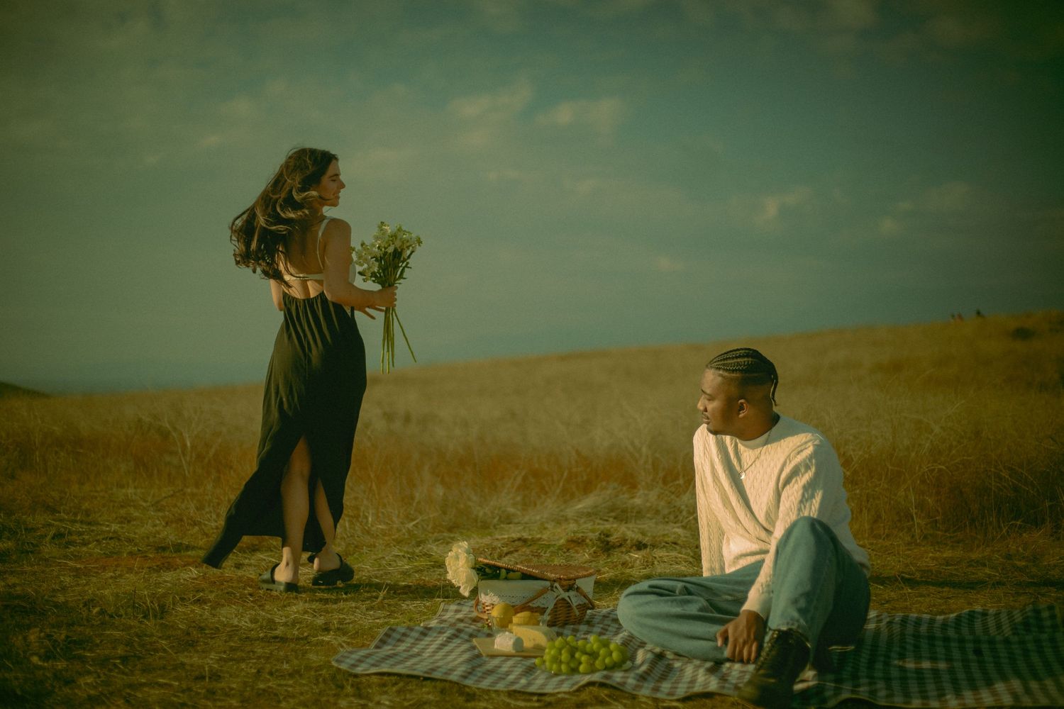 Romantic couple enjoying a picnic on a blanket in a grassy field in Riverside California under a moody overcast sky.
