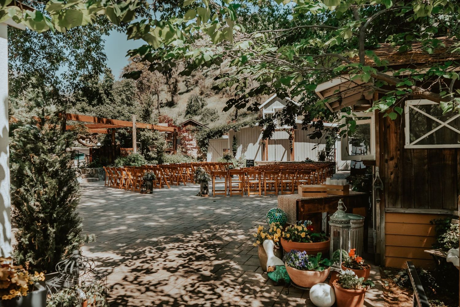 Rustic outdoor wedding ceremony setup with wooden chairs and autumn decorations in a sunlit garden venue.