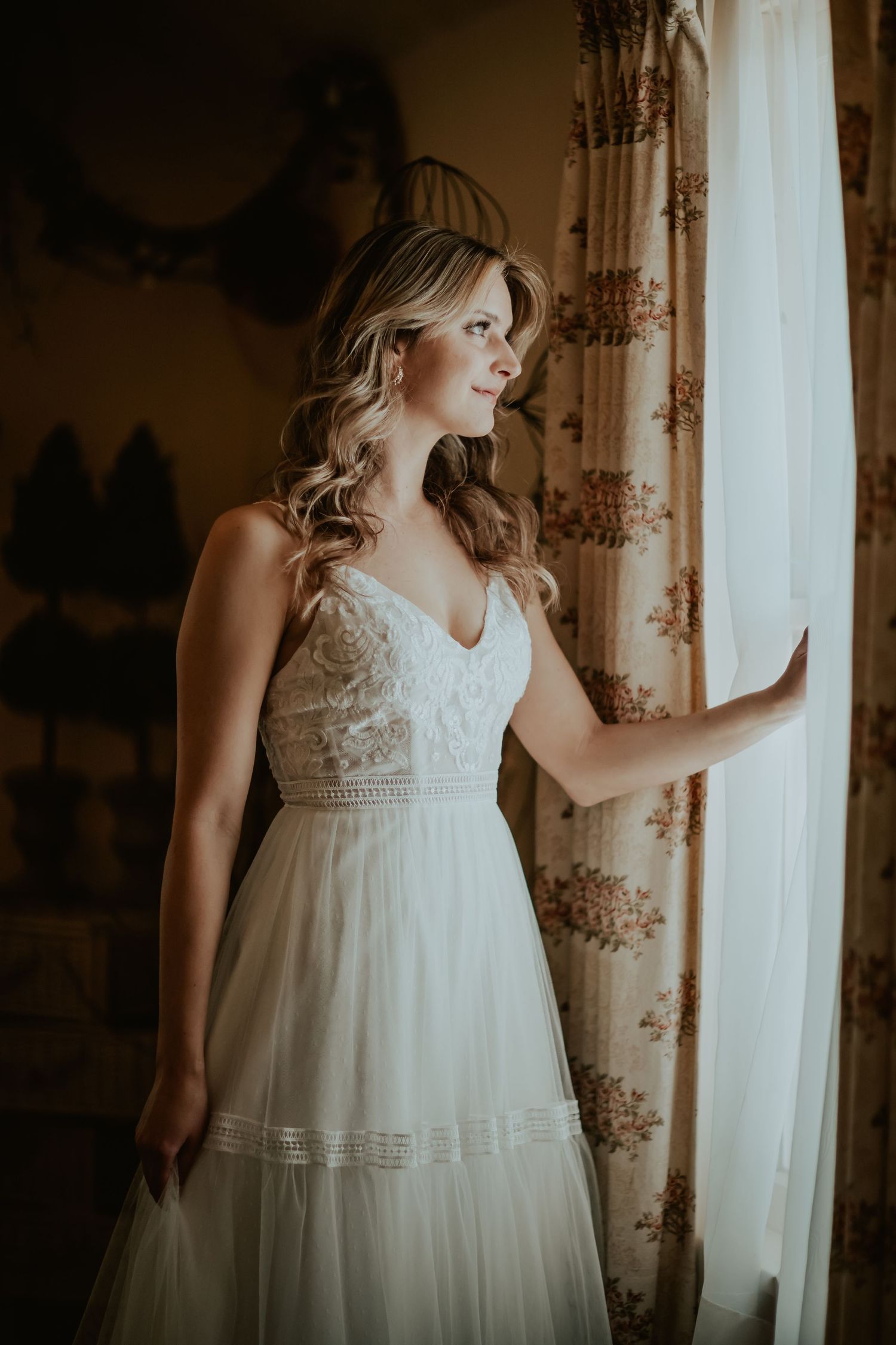 Elegant white wedding dress with lace bodice and flowing tulle skirt captured in moody window light.