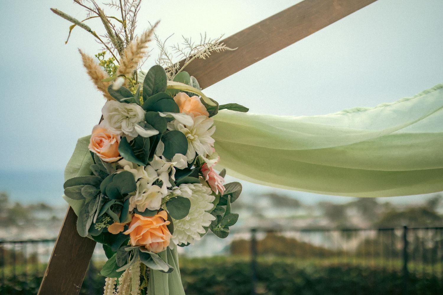 Floral wedding arch decoration with peach roses and flowing mint green fabric against a blurry city backdrop.
