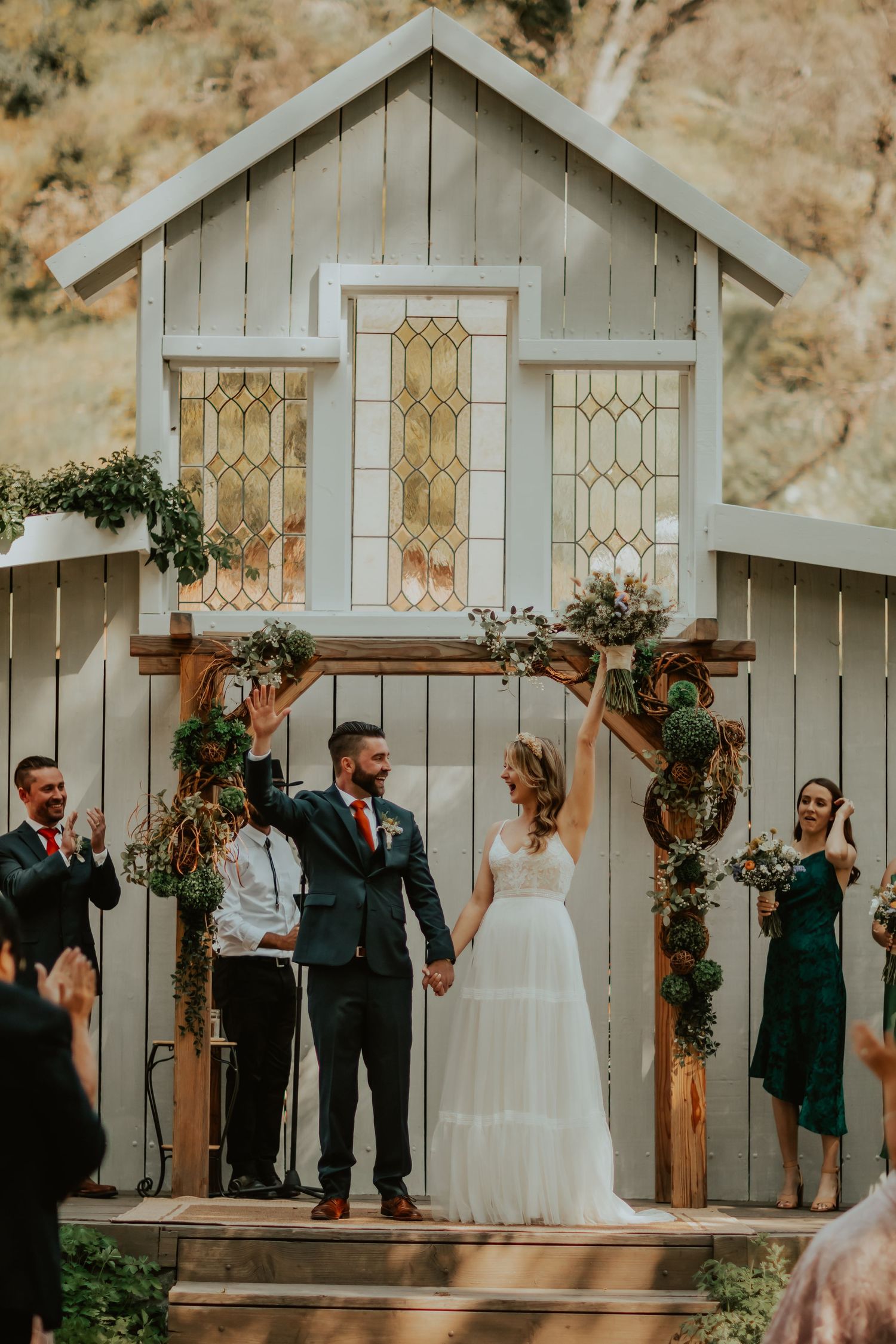 A wedding ceremony at a charming white chapel with stained glass windows and floral arch decorations during golden hour.