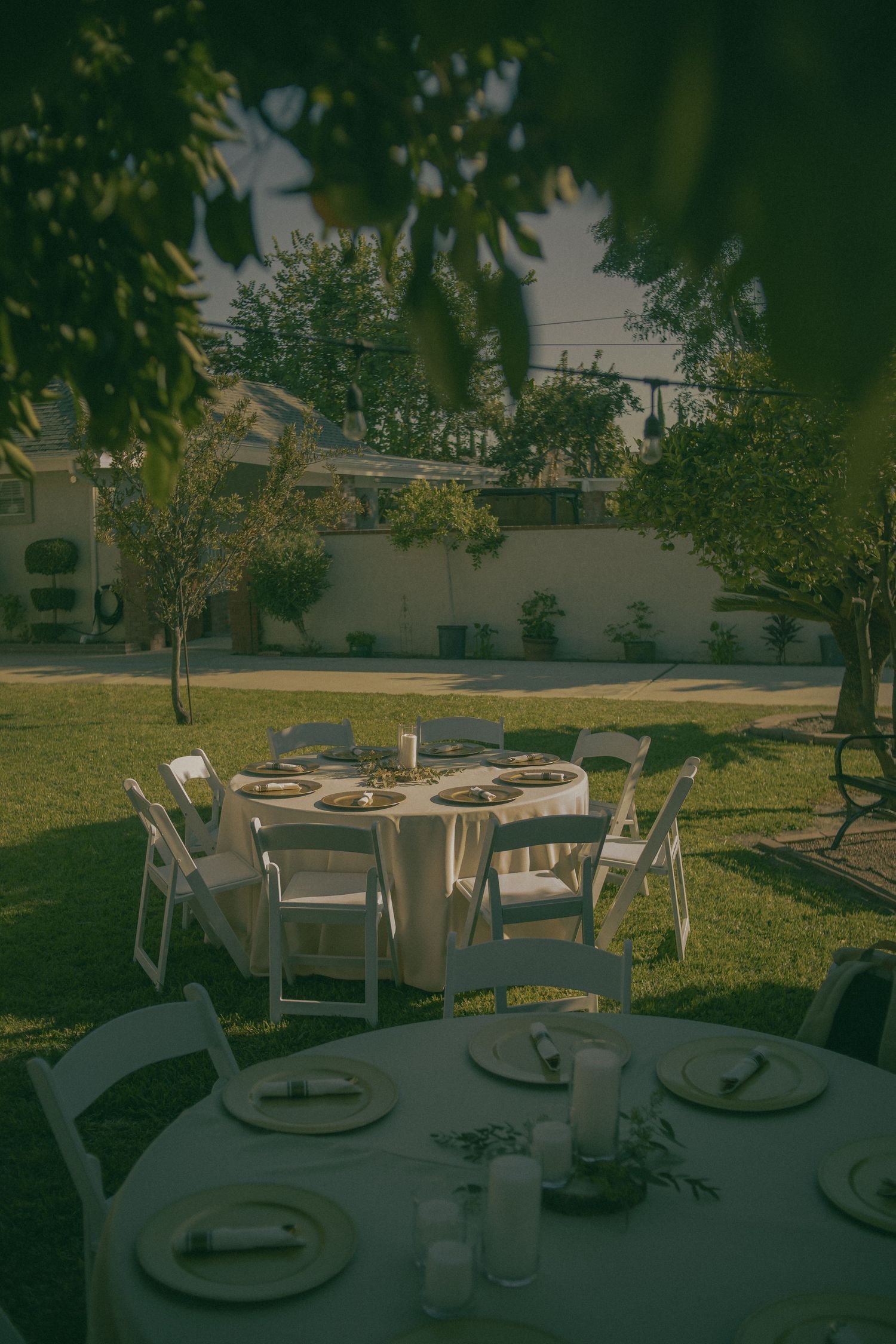 Outdoor wedding reception setup with round tables and white chairs in a green garden in Chino California