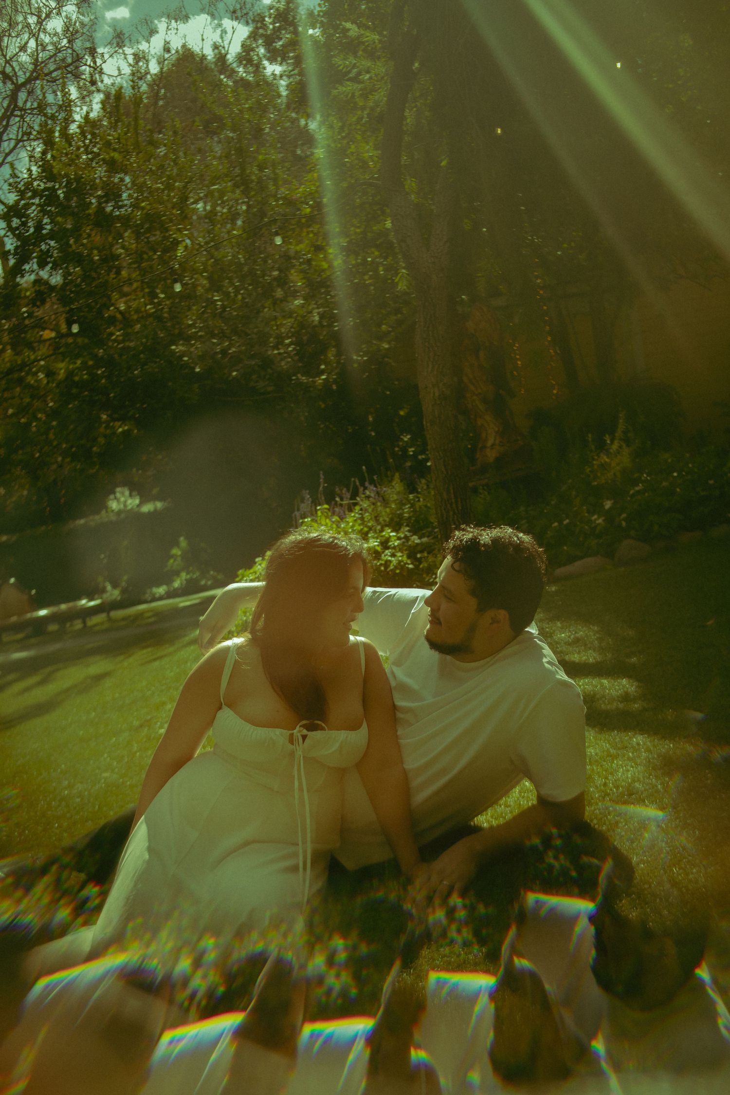 A couple sits intimately together on a blanket in a sunlit garden with dreamy lens flares in the foreground in San Diego, California