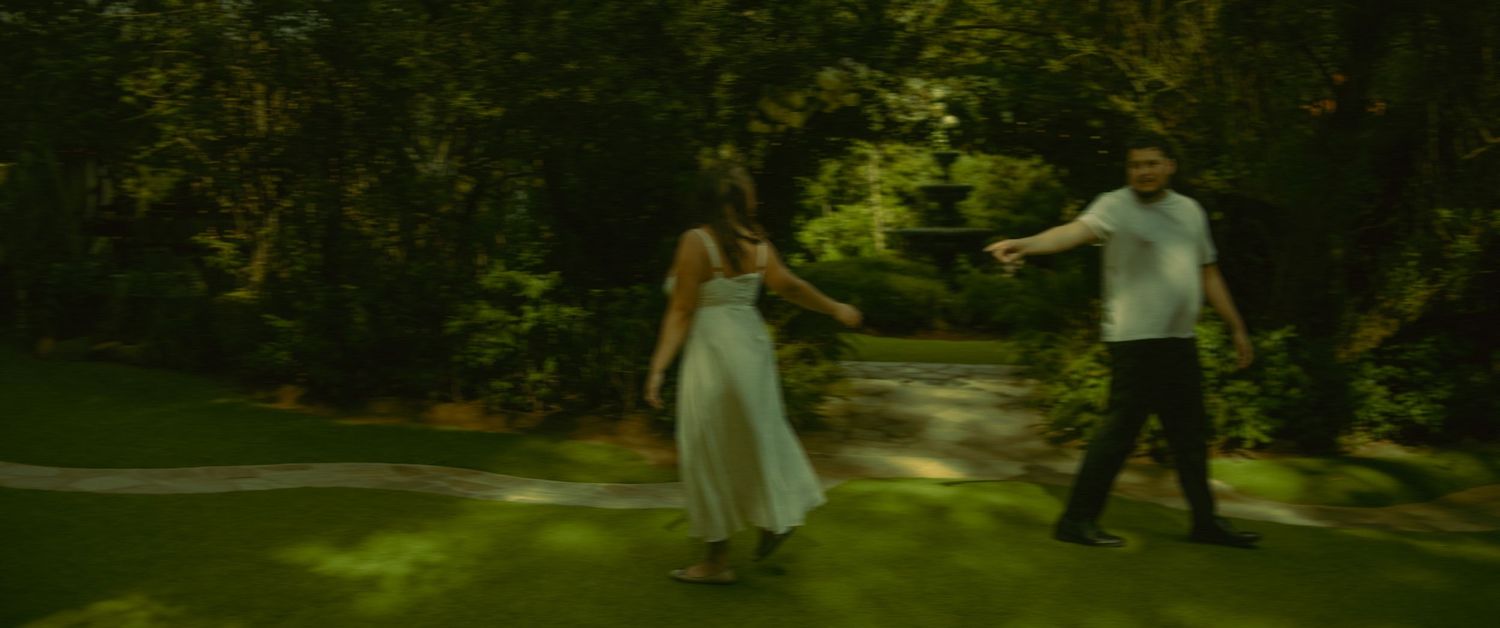 A couple dances together on a sun-dappled garden path surrounded by lush green foliage for their engagement shoot in Twin Oaks, California