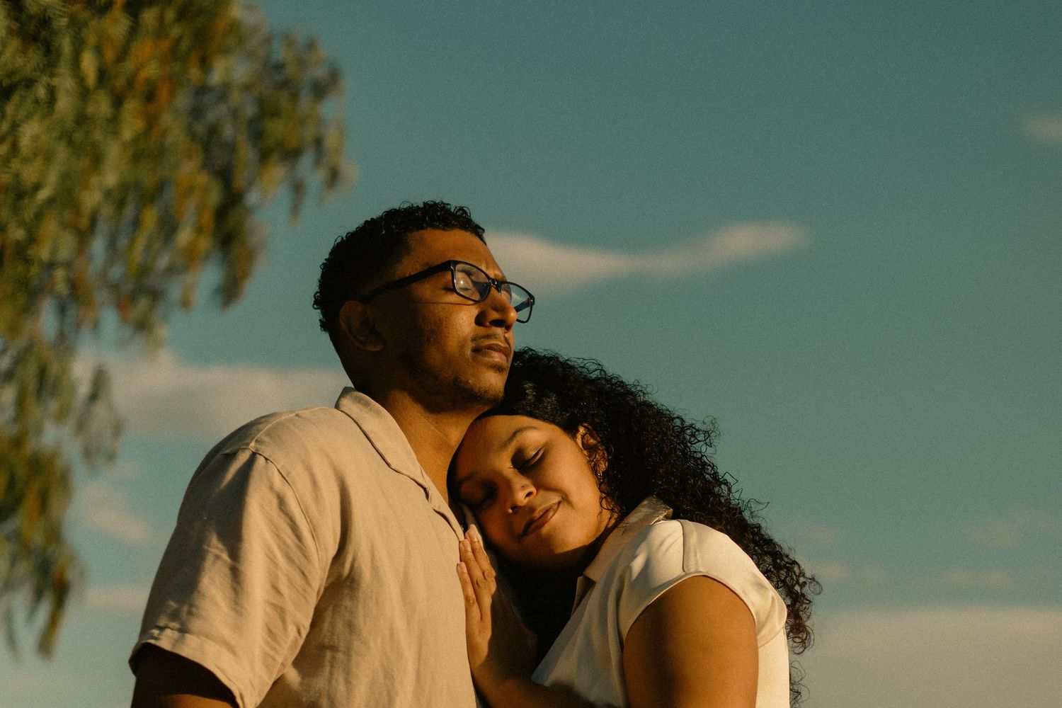 A loving couple share a tender movie like moment together against a blue sky with golden sunlight during their photoshoot in Chino Hills