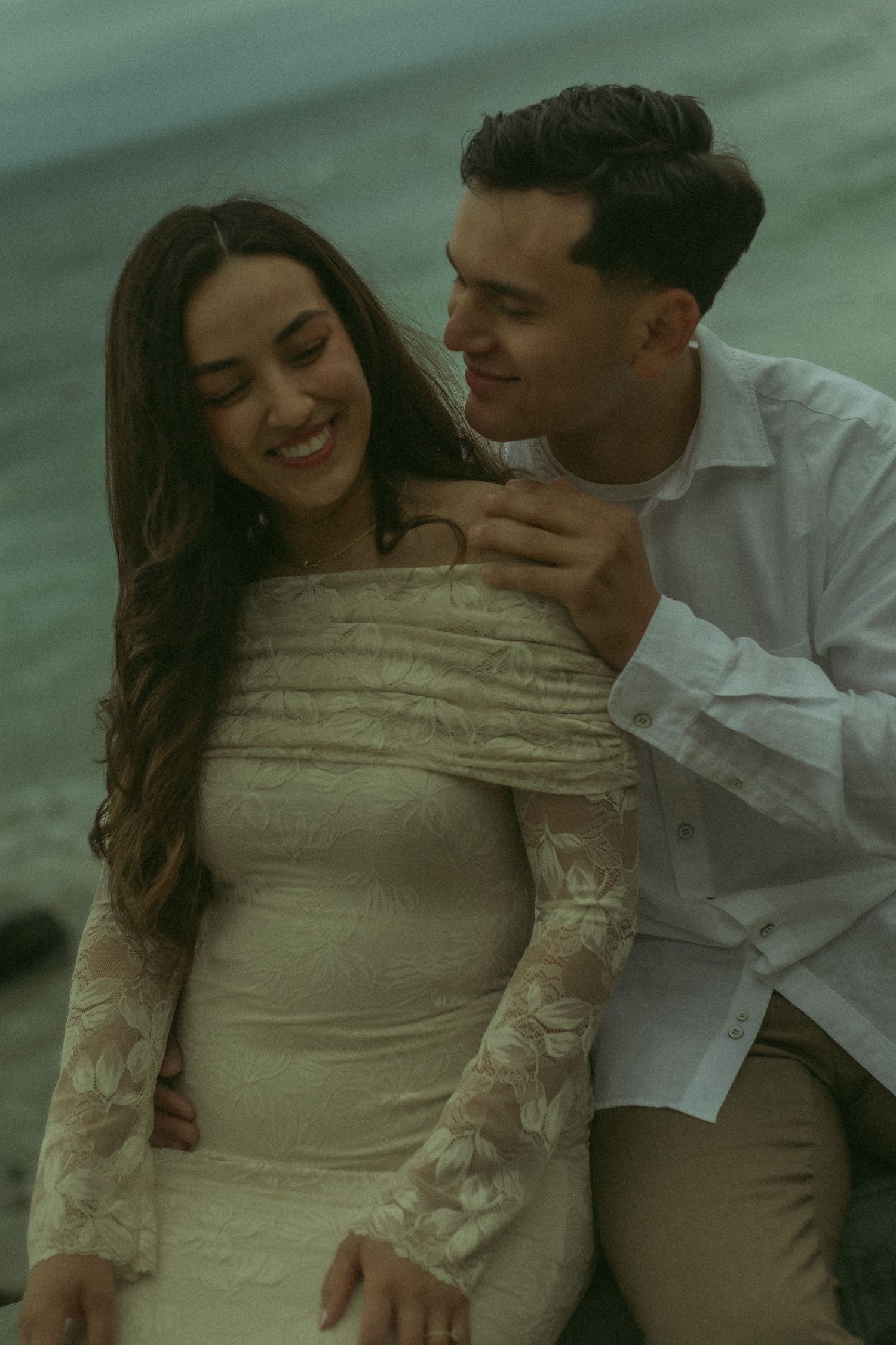 Couple laughing together while sitting on a bench at the beach.