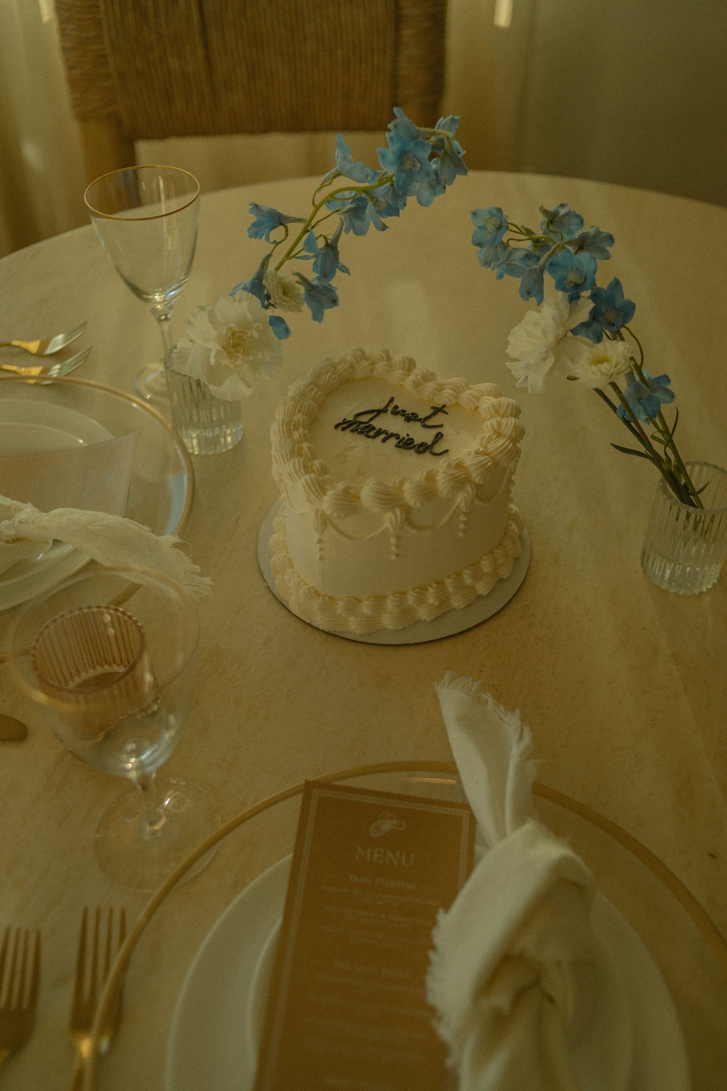 An elegant table setting with a white frosted cake and blue delphinium flowers in vases on the wedding cake table