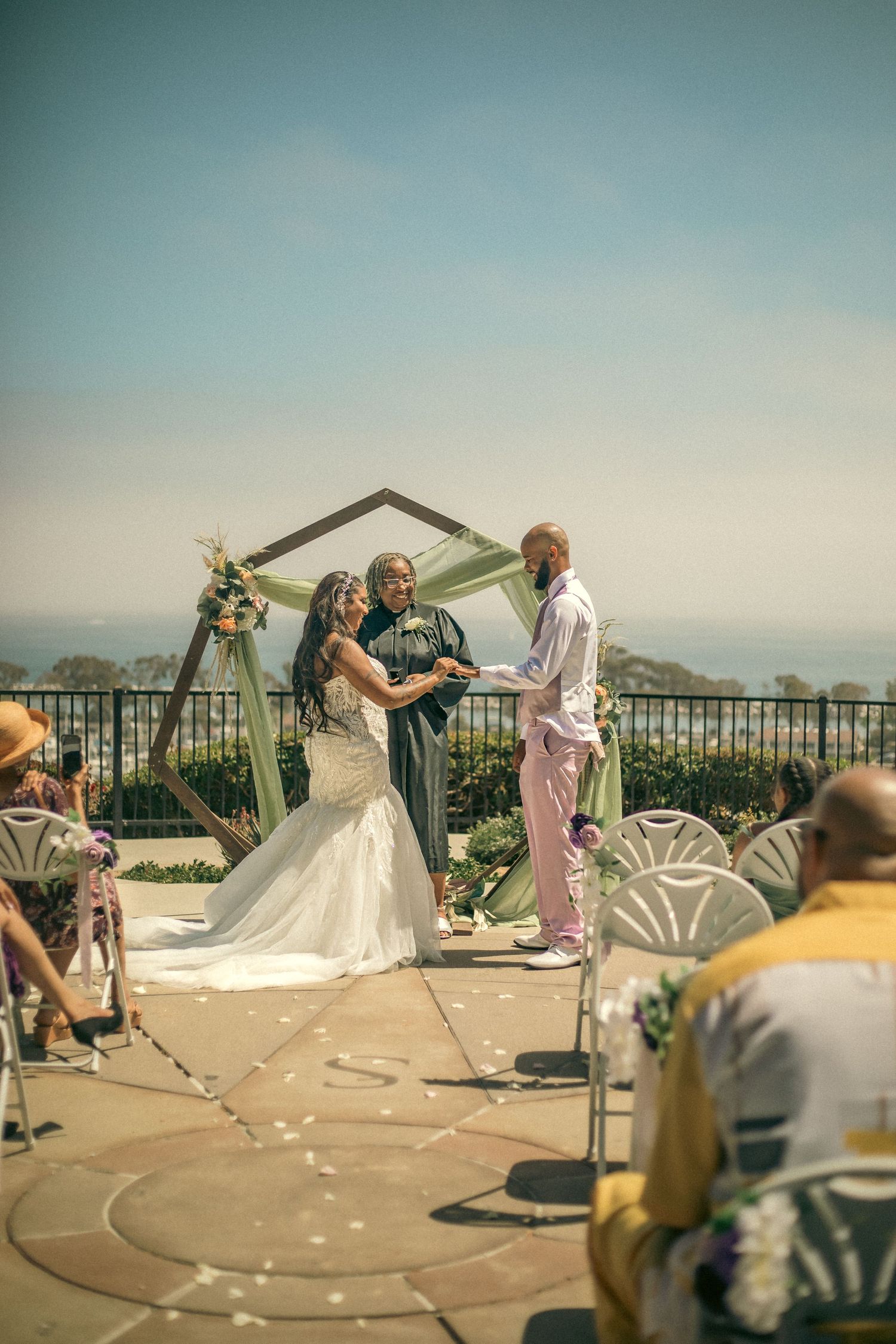 A wedding ceremony takes place on an outdoor terrace overlooking the scenic ocean view