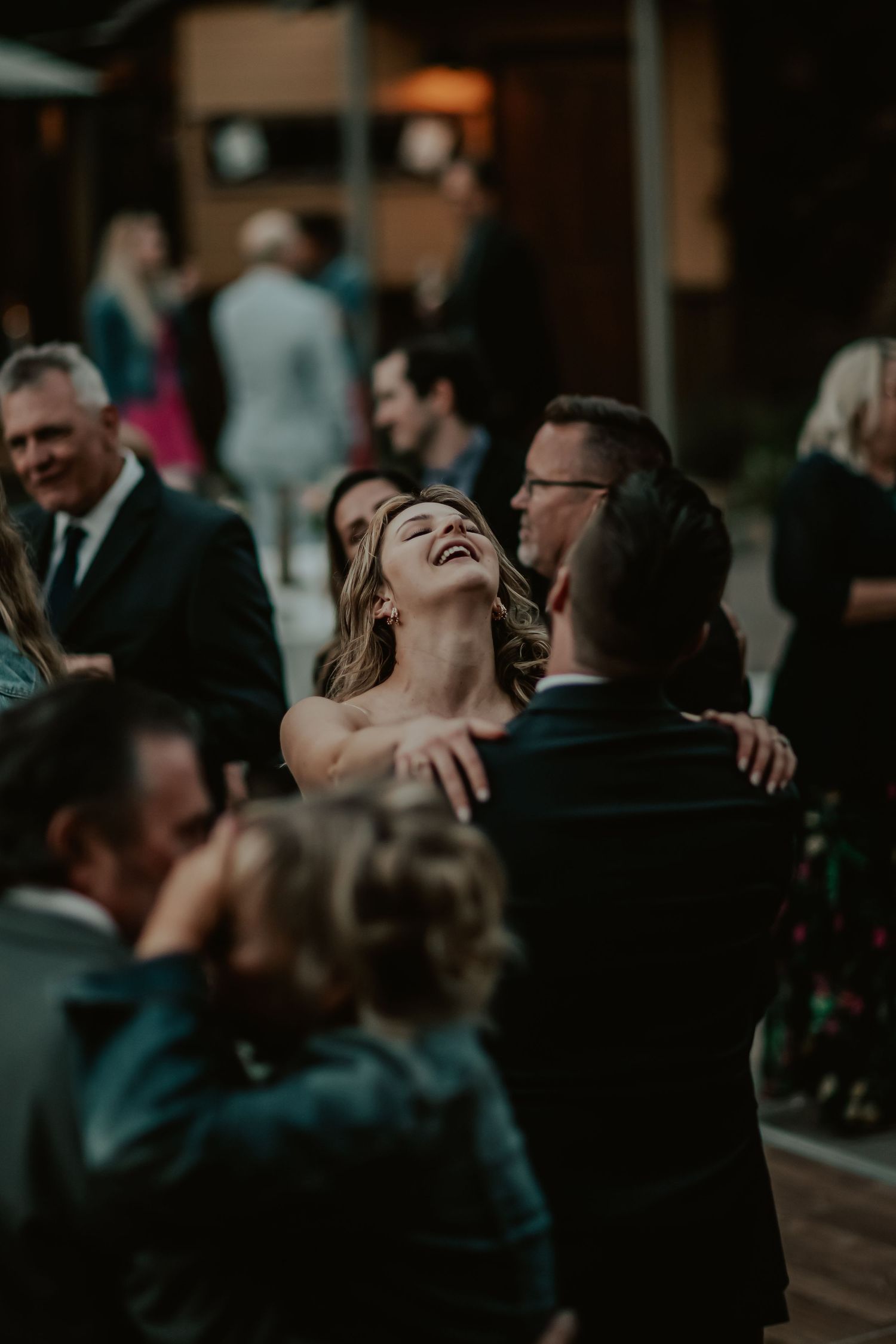 A couple shares a joyful moment dancing on the wooden floor during an evening wedding reception.