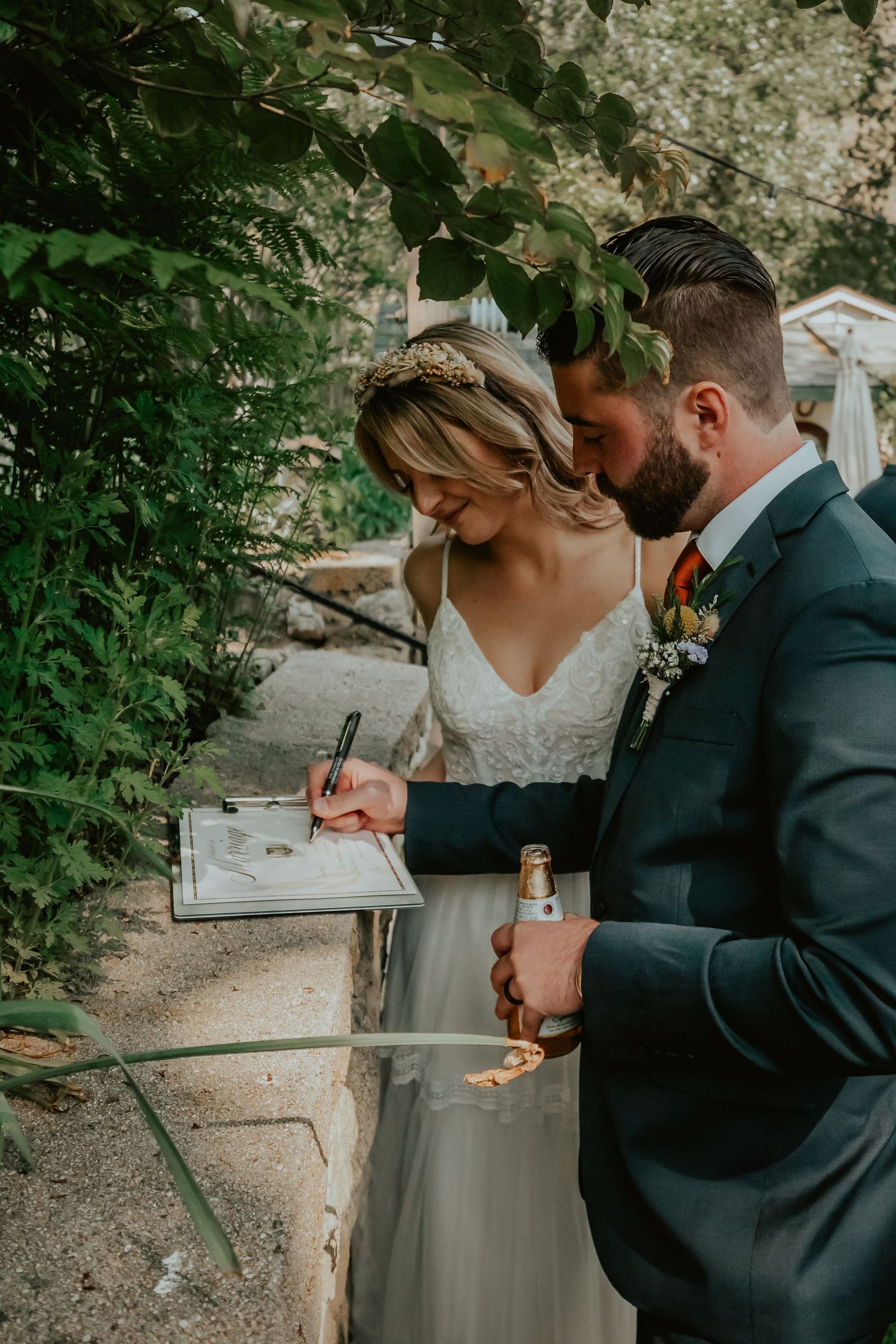 Newlywed couple signing marriage documents outdoors during intimate garden wedding ceremony.