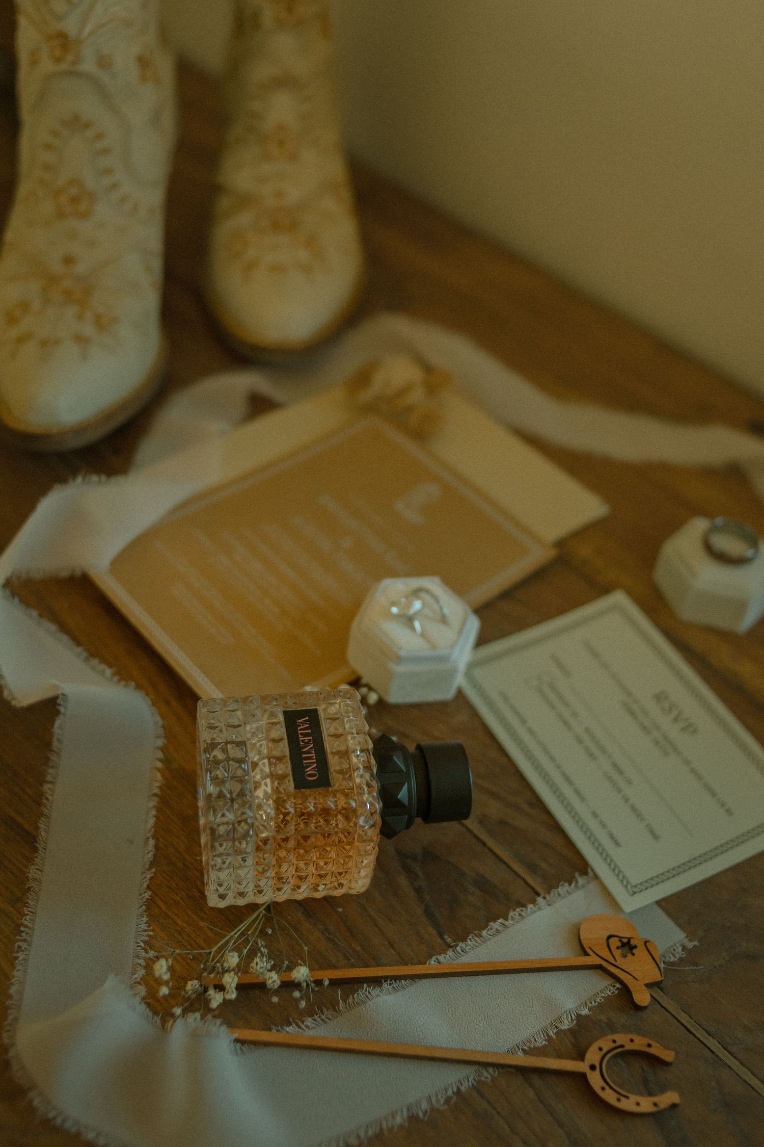 Wedding details including vintage boots, documents, perfume bottle, and antique key on rustic surface in warm lighting.