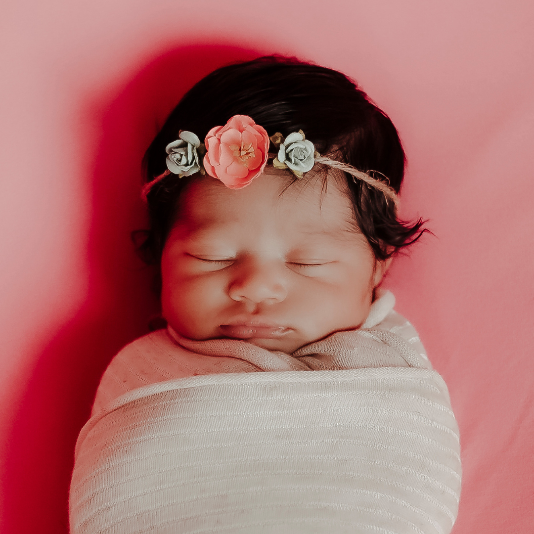 Sleeping newborn baby wrapped in white swaddle wearing delicate floral headband for their newborn photography session