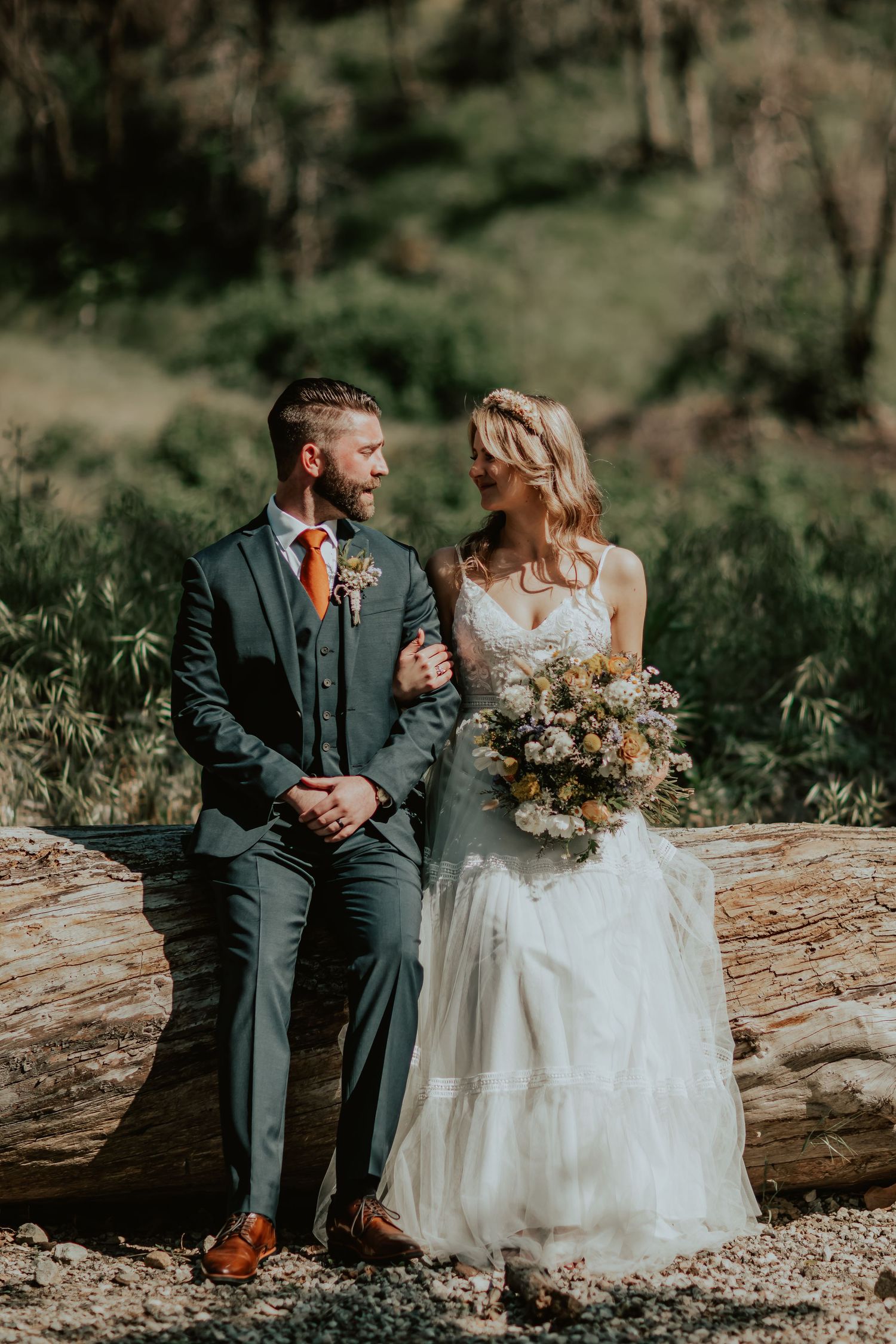 Bride and Groom sitting on a fallen tree trunk in a mountain wedding venue setting