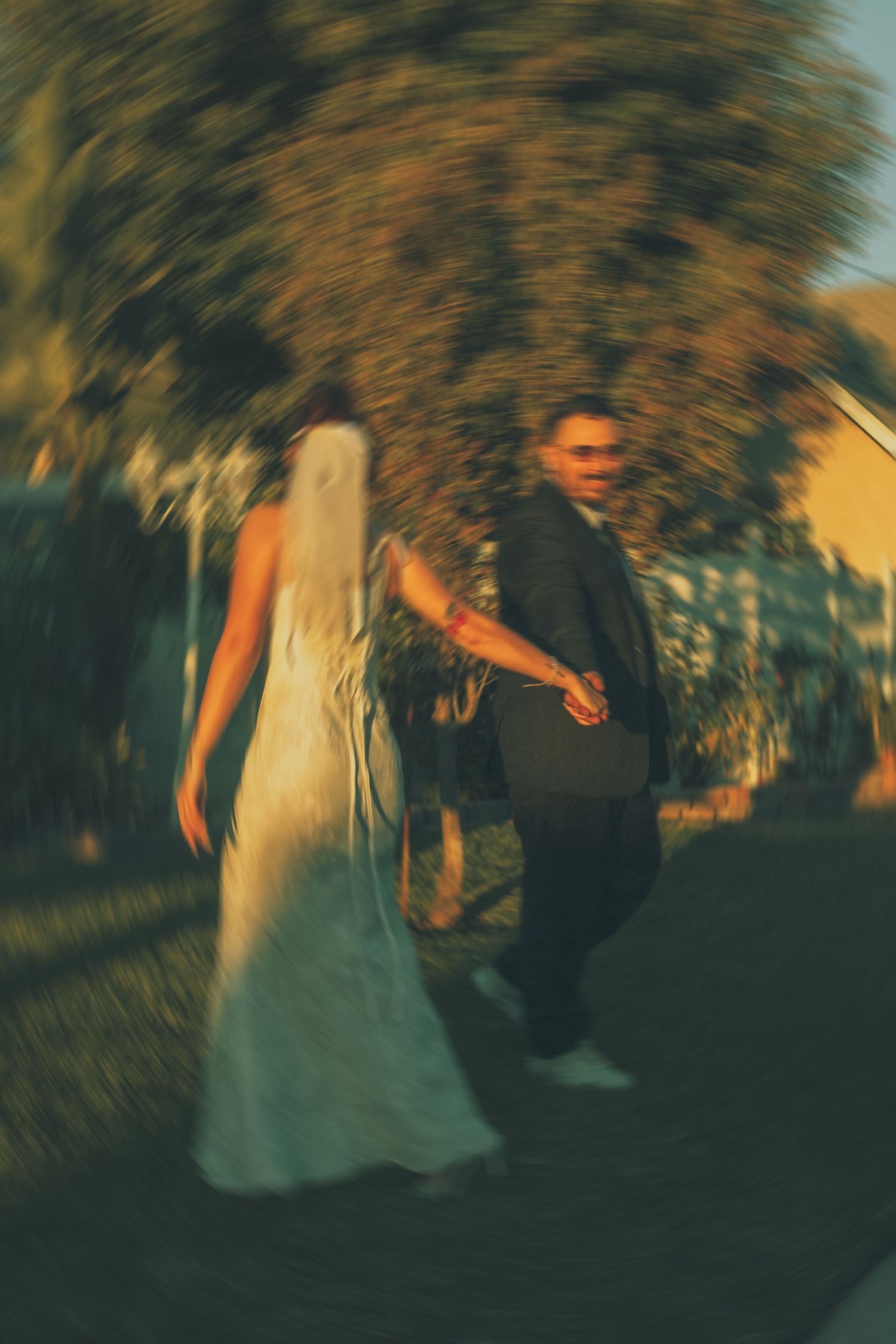A couple in wedding attire dance together at dusk in an artistic blurred motion photograph.