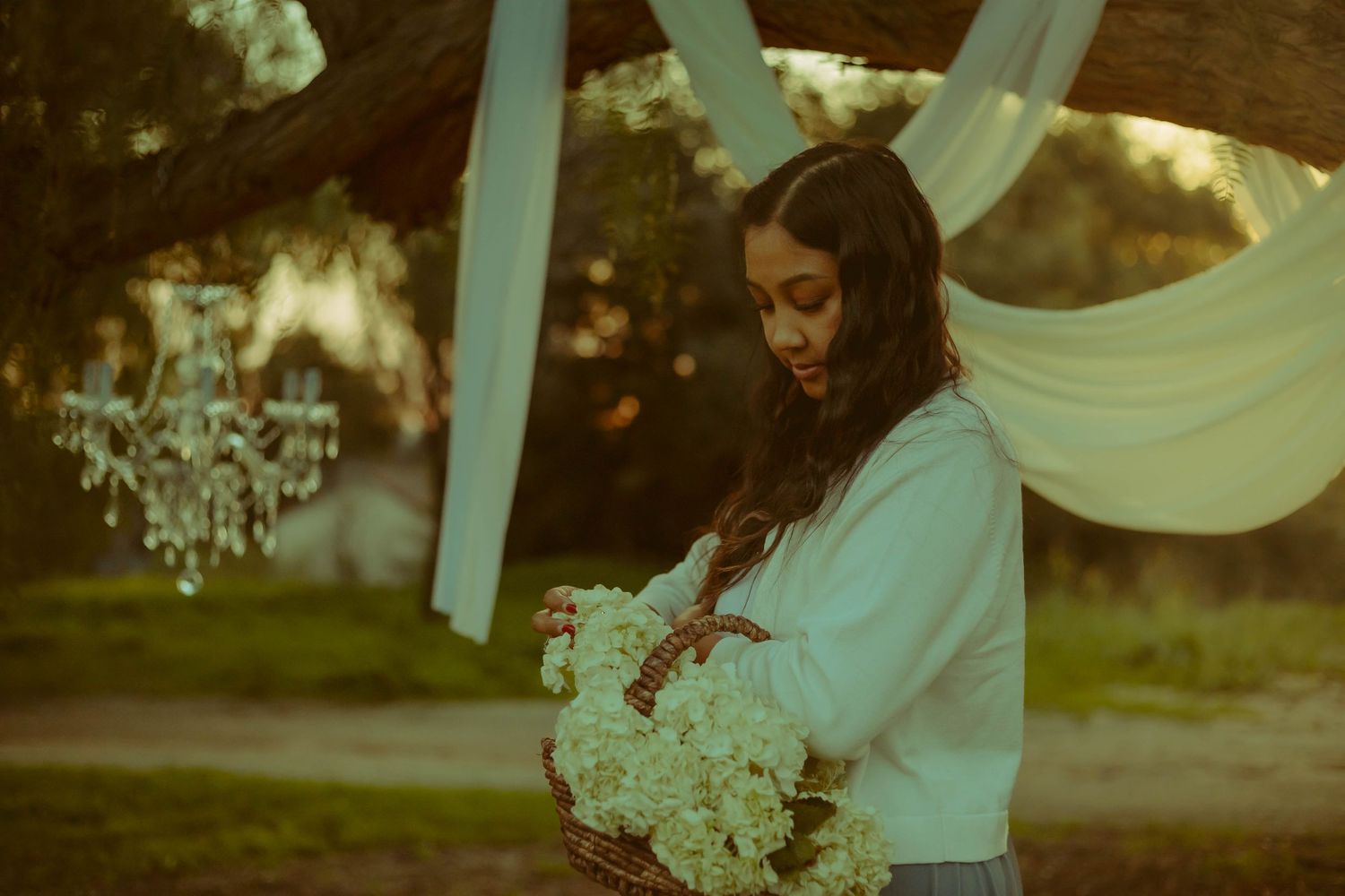 Ethereal mini session with flowing white fabric and delicate flowers illuminated in soft dreamy light beneath ornate chandelier in SoCal.