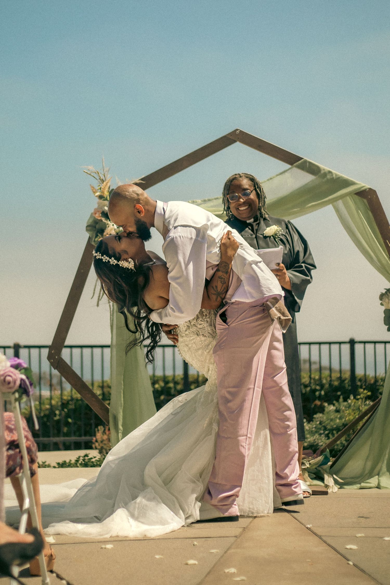 A romantic celebration moment at an outdoor wedding ceremony under a geometric arch with draped fabric.