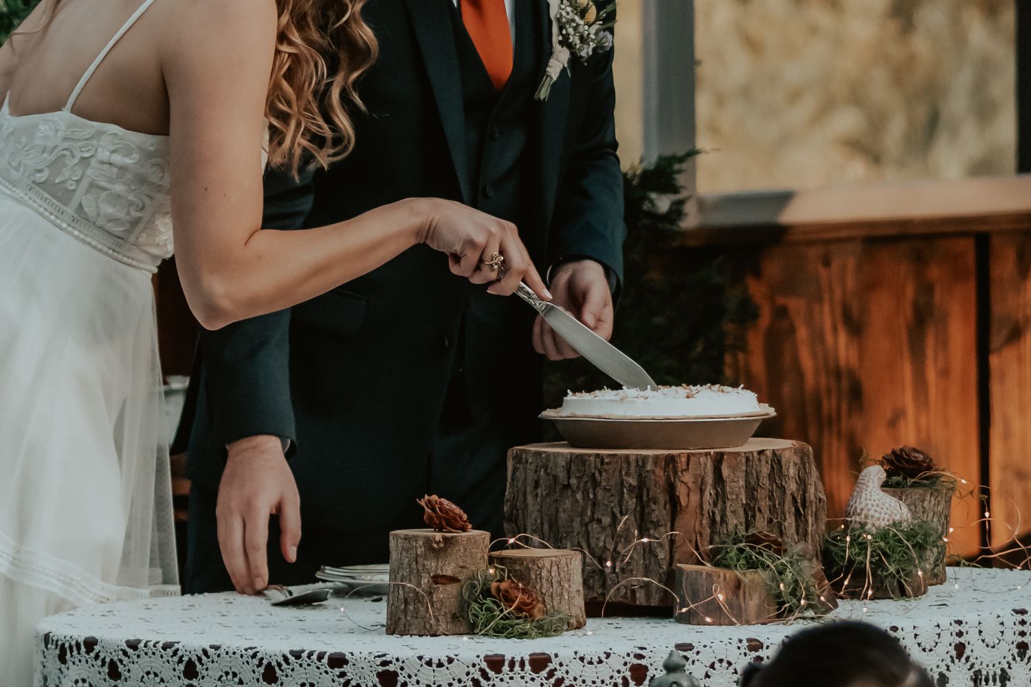 A couple cutting their rustic wedding pie displayed on a wood slice at an outdoor reception.