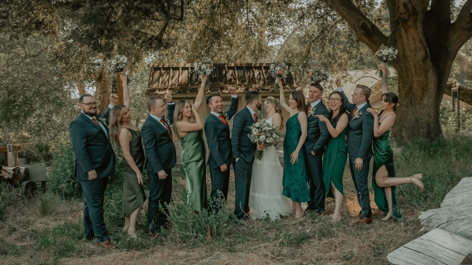 A wedding party in navy suits and emerald green dresses poses playfully together at The Homestead in Oak Glen