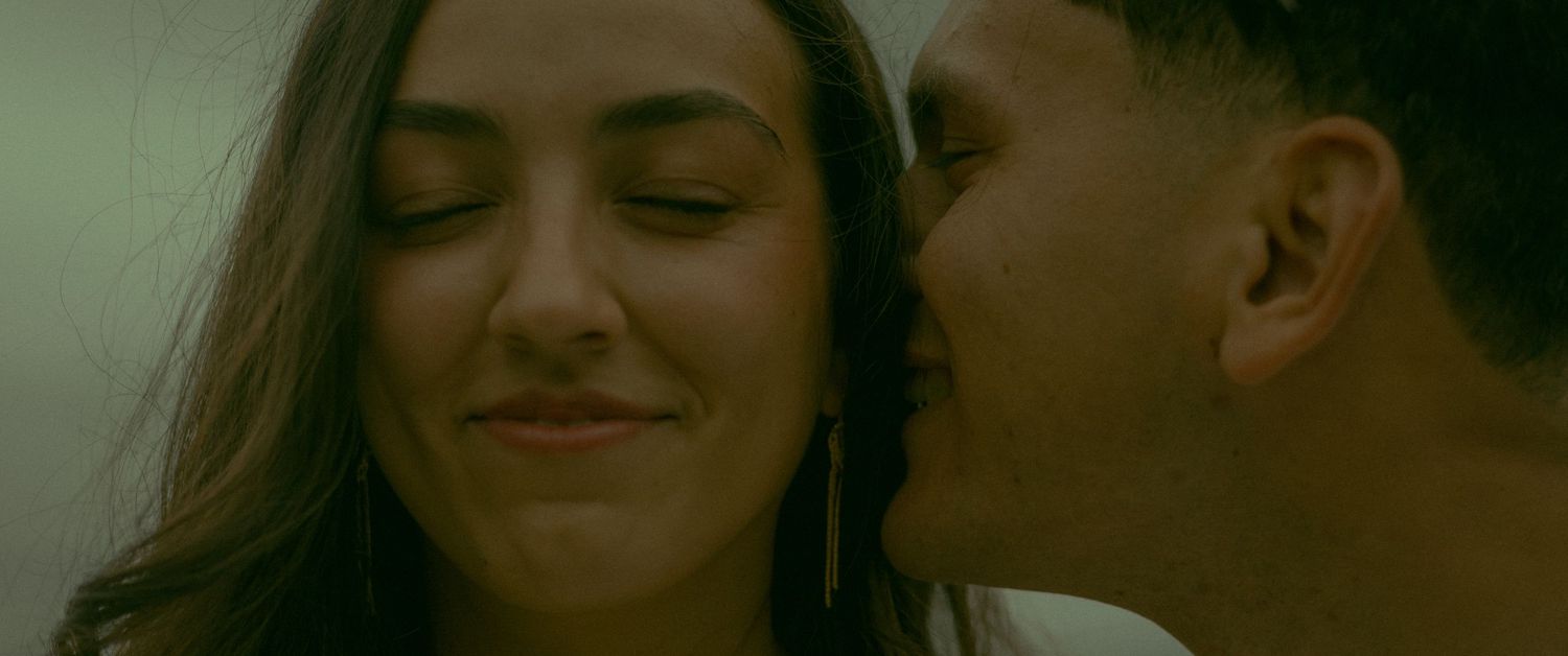 Husband whispering loving secrets into his wife's ear as the waves crash behind them.