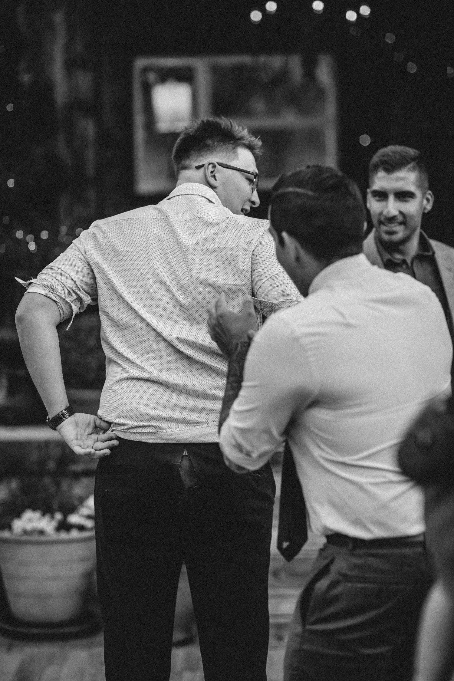 Three people having an animated conversation about the ripped pants at the wedding in black and white photography.
