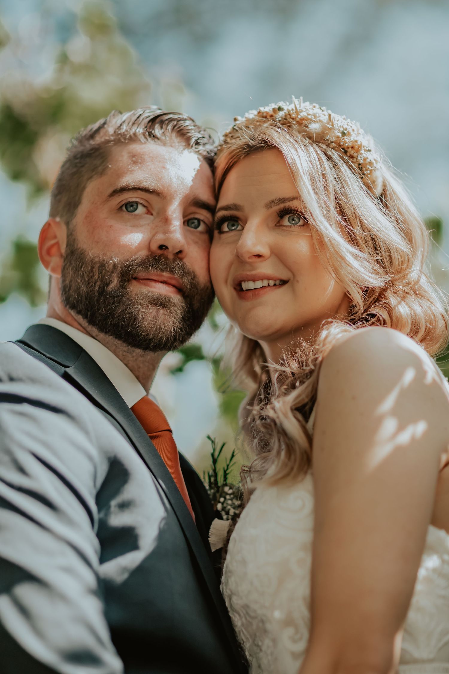 A happy couple pose together on their wedding day in a natural outdoor setting with soft bokeh lighting effects.