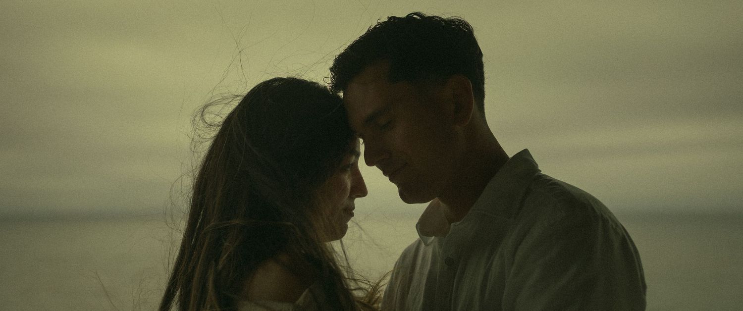 Couple standing forehead to forehead in a romantic embrace on the cliffside of a California Beach.