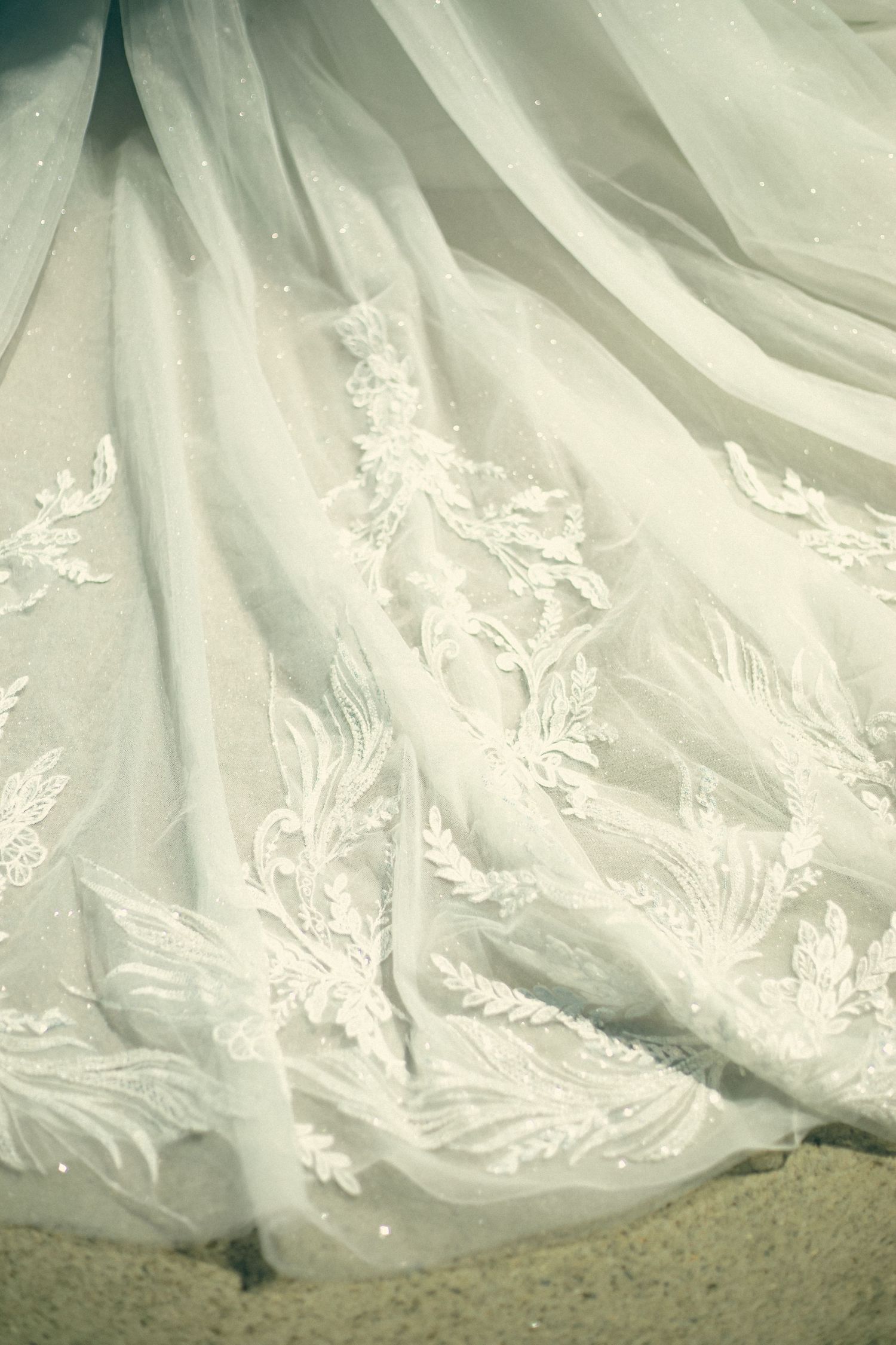 Delicate white lace and embroidery details adorn the flowing fabric of an elegant wedding dress hem.