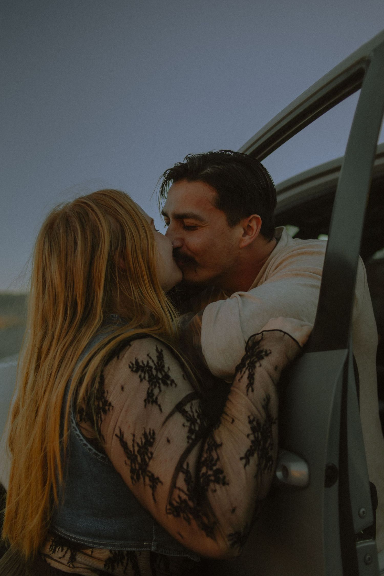 Couple kisses through a truck window for their couple session located in the desert of Joshua Tree, California