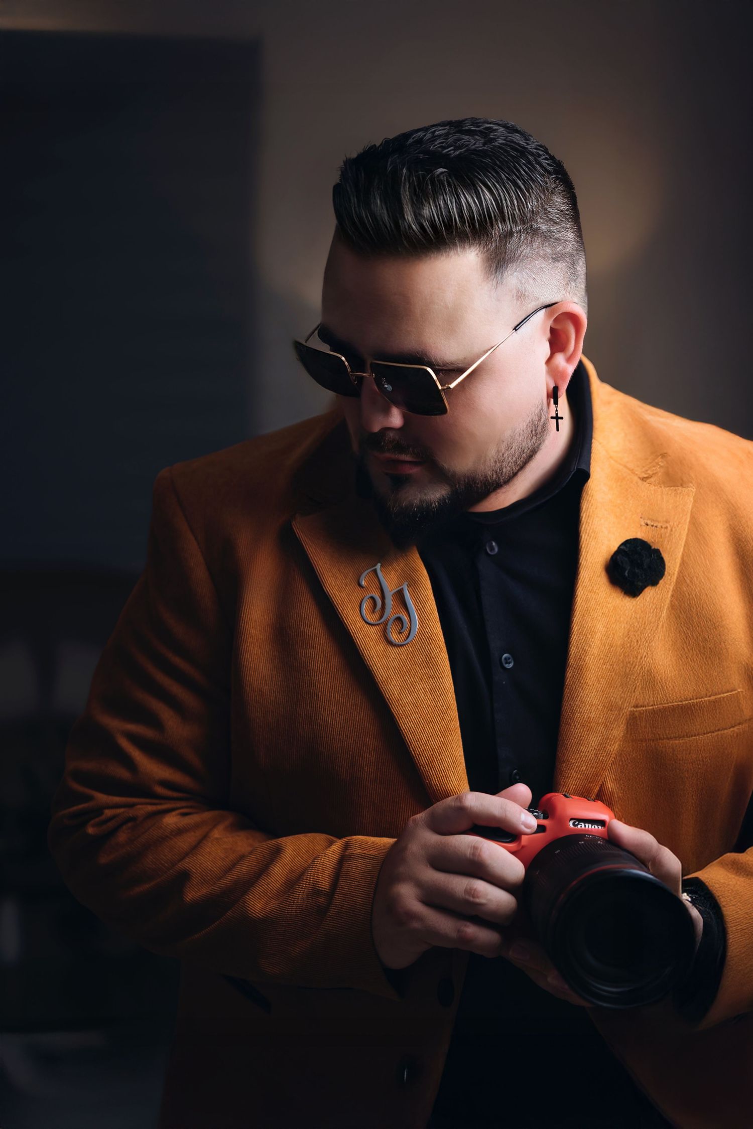 Photographer in orange blazer and sunglasses holding camera in moody lighting setup.