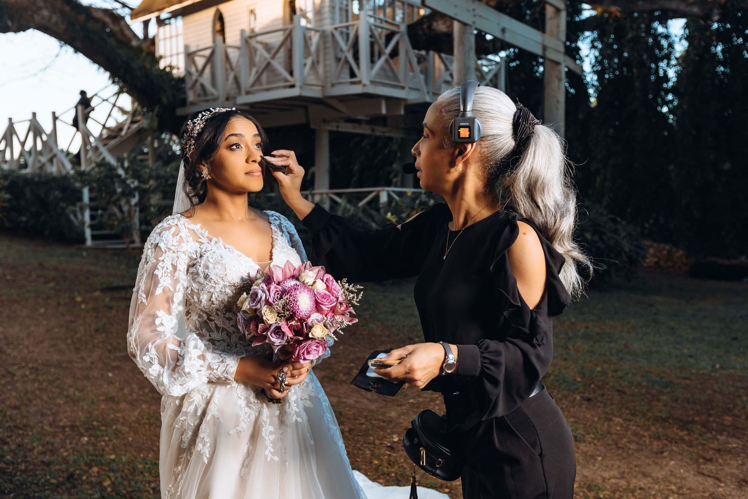 Wedding preparation scene outdoors with pink bouquet and dress details being finalized.