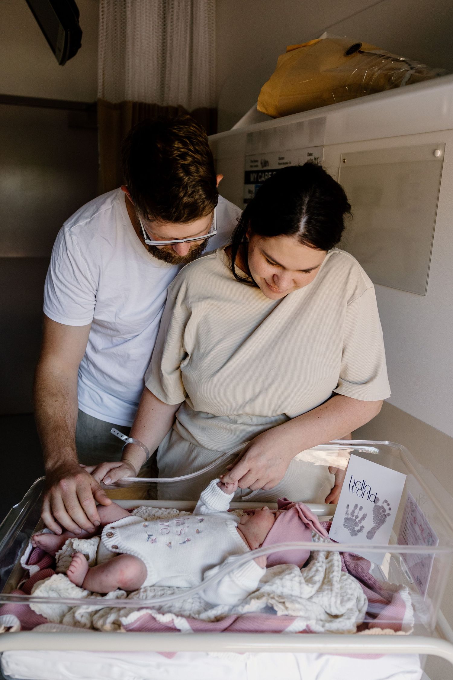 A couple changes their baby's diaper on a white changing table, leaning in together during the intimate parenting moment.