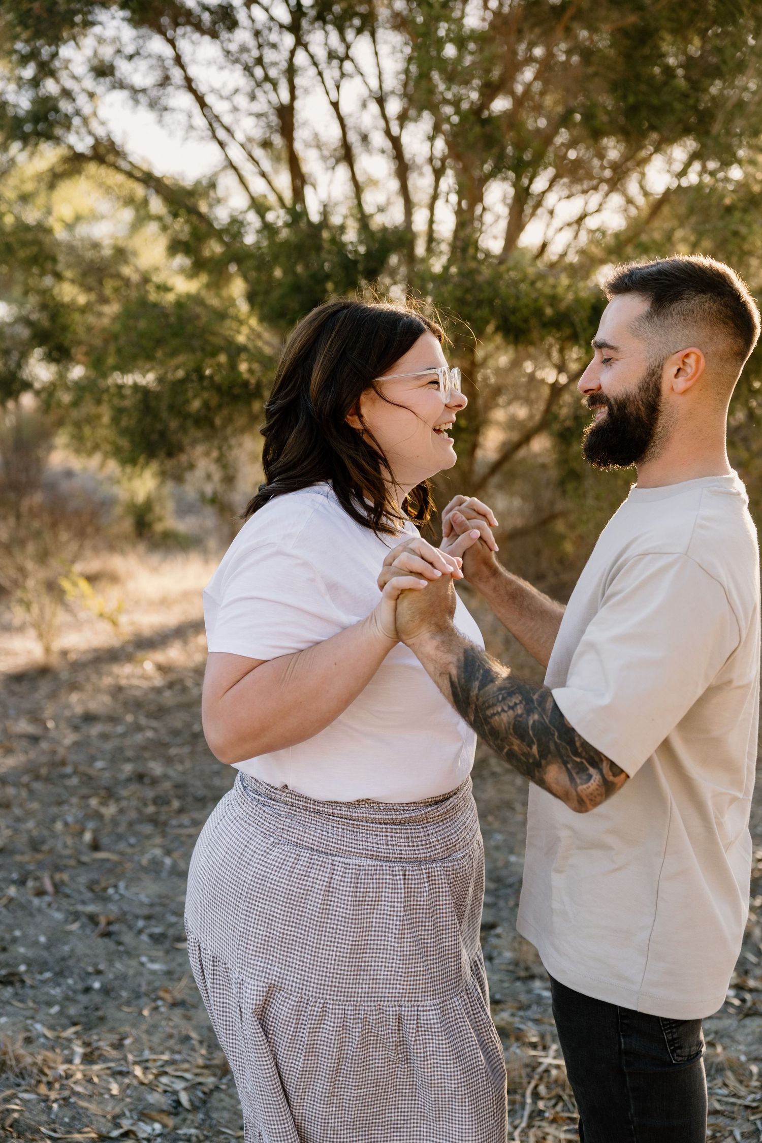 A joyful couple shares a tender moment outdoors against a backdrop of trees at golden hour.