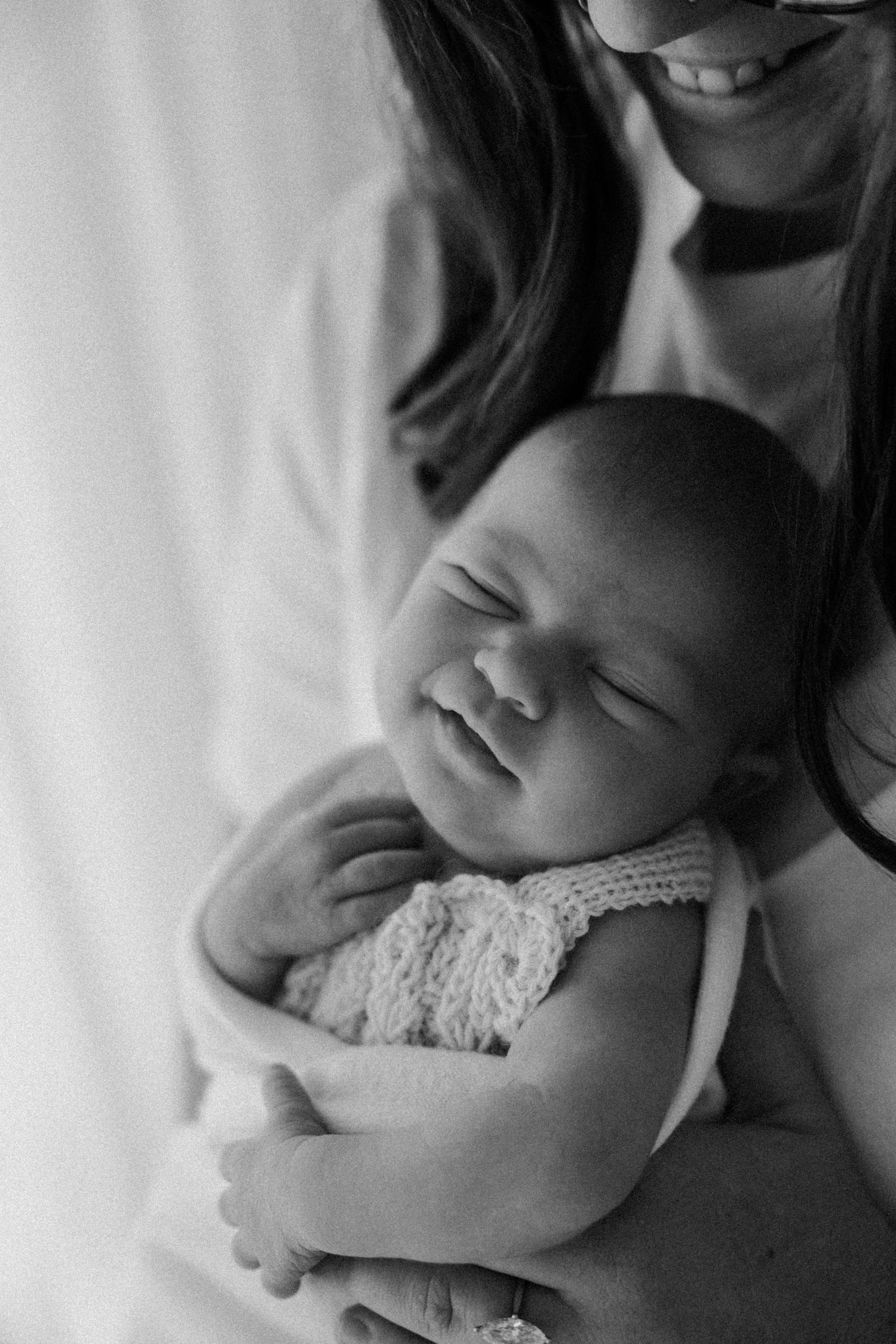 Black and white portrait of a peaceful sleeping newborn in a lace outfit being held against a white background.