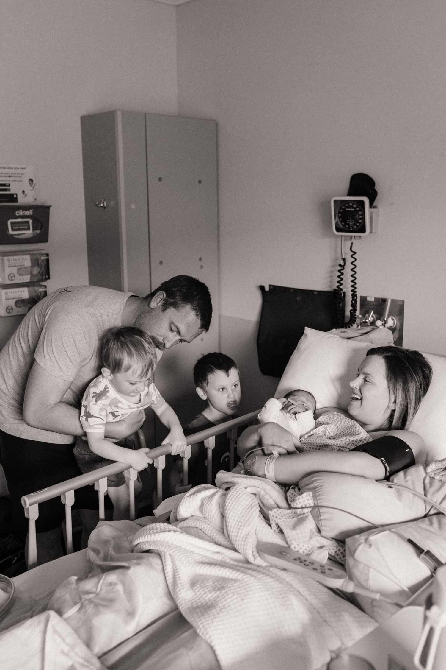 A tender black and white hospital room scene shows a family gathering around a hospital bed with pillows and medical equipment.